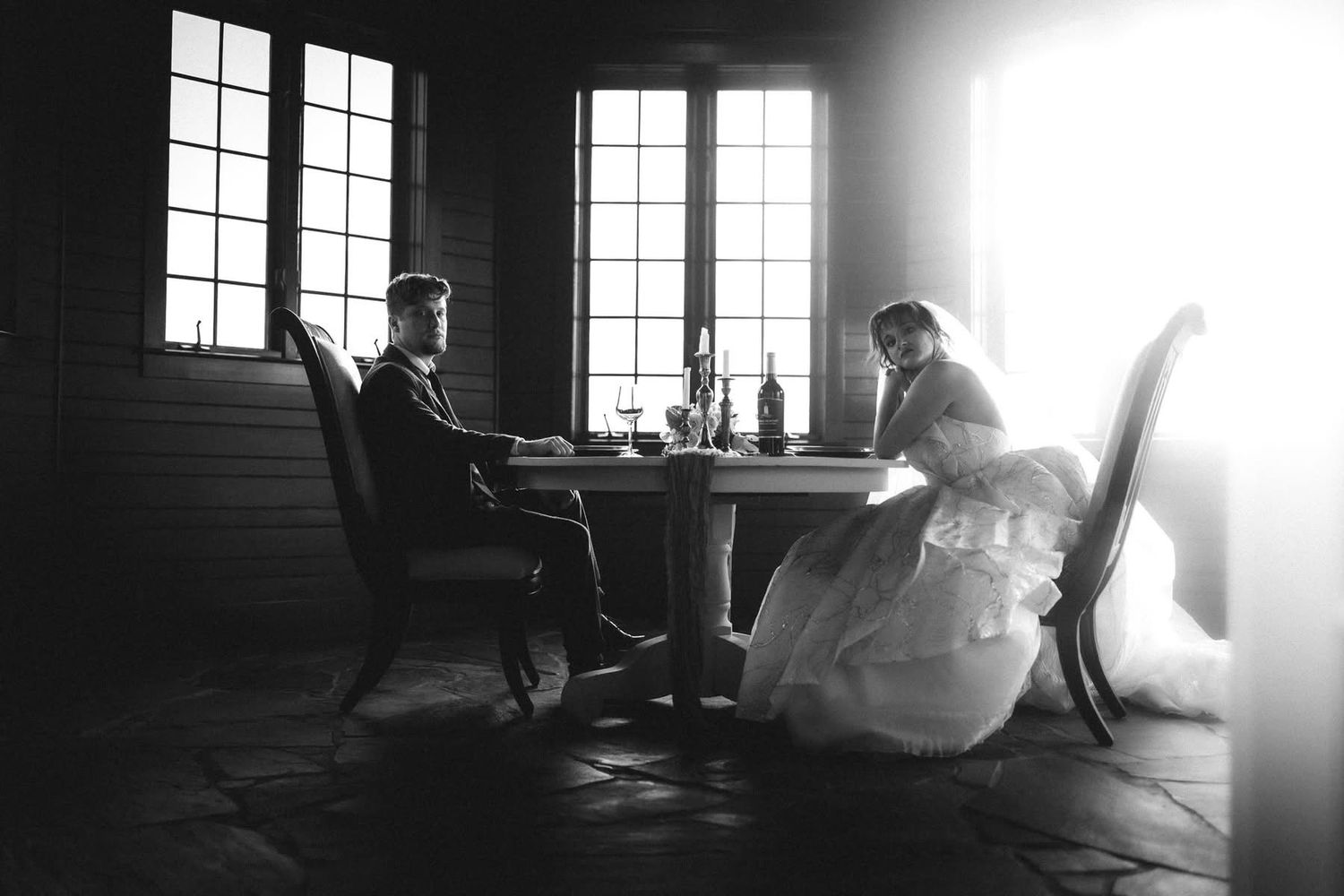 Bride and groom sit at table in moody black and white wedding photo.