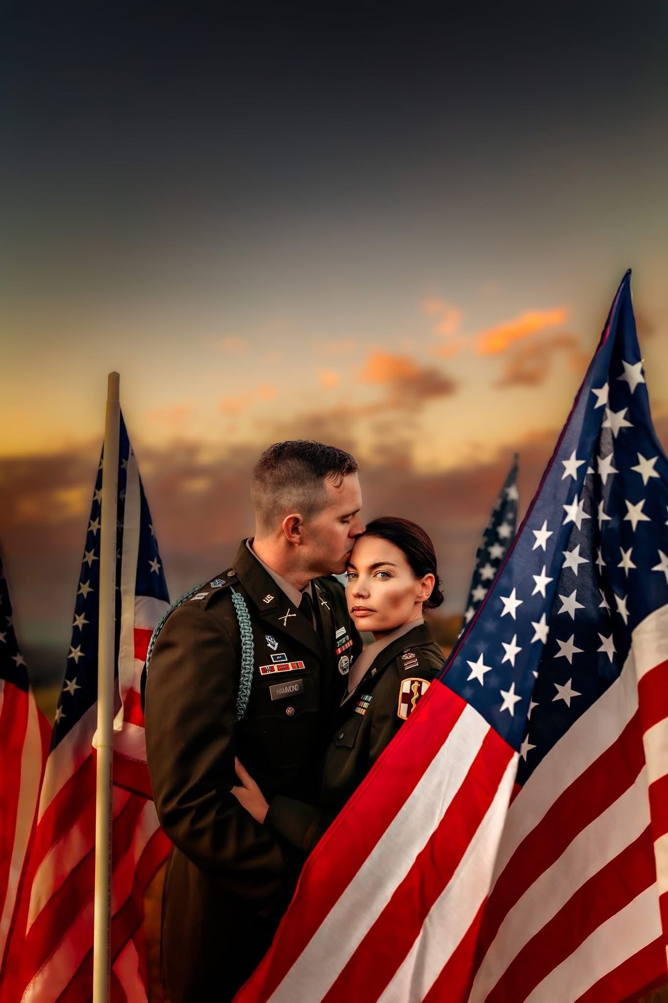 Two U.S. soldiers share a tender moment surrounded by American flags at sunset.
