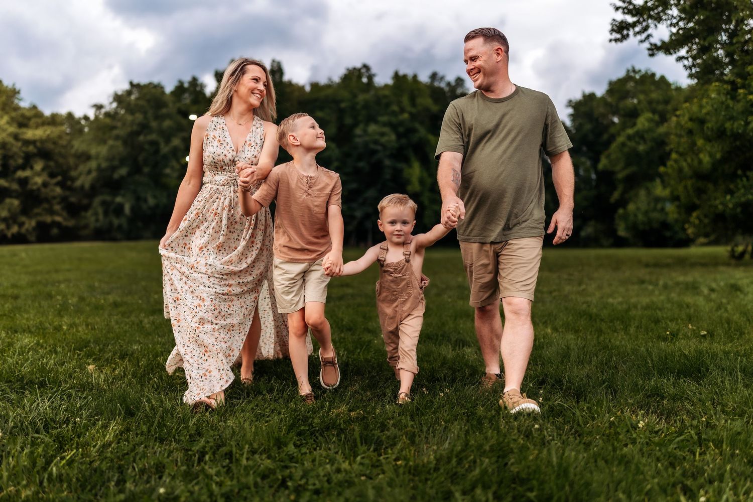 Happy family of four walking barefoot on green grass in a park on a cloudy day.