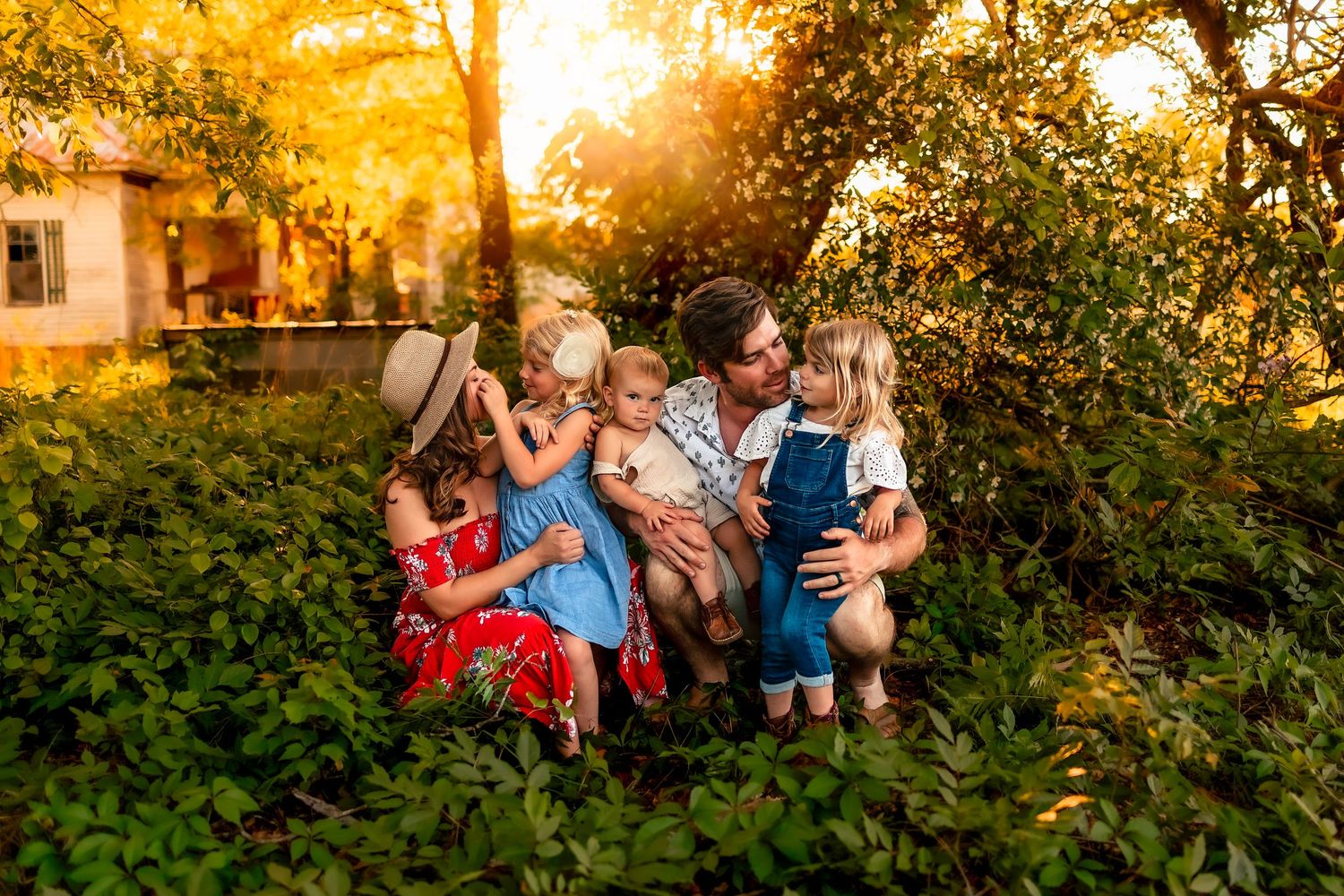 Family of five sitting together in lush green garden during golden hour sunset photography session.