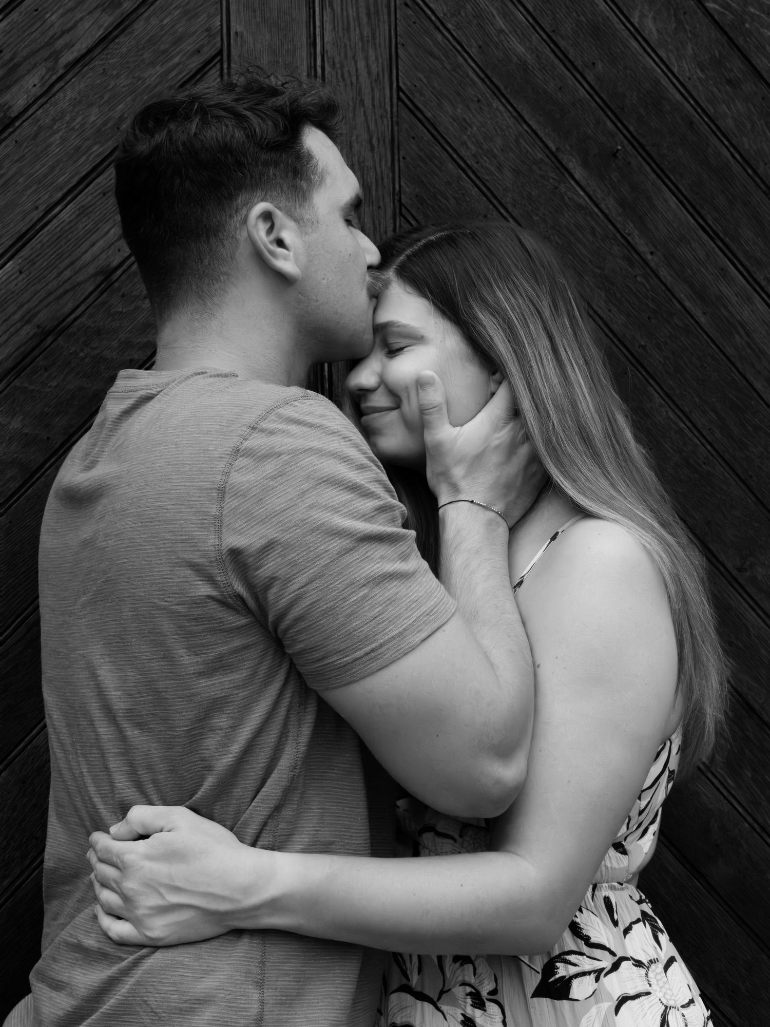 Black and white photo of a romantic couple embracing, man kissing woman's cheek while she smiles softly.