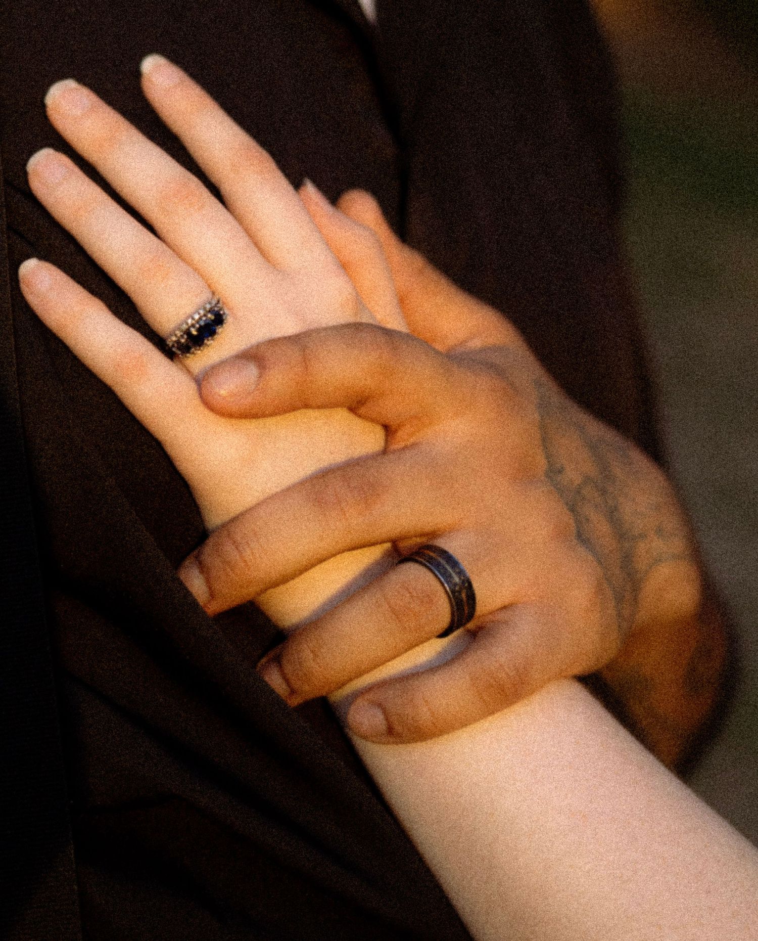 Close-up of two hands held together, each wearing a black ring, with a tattoo visible on one wrist.