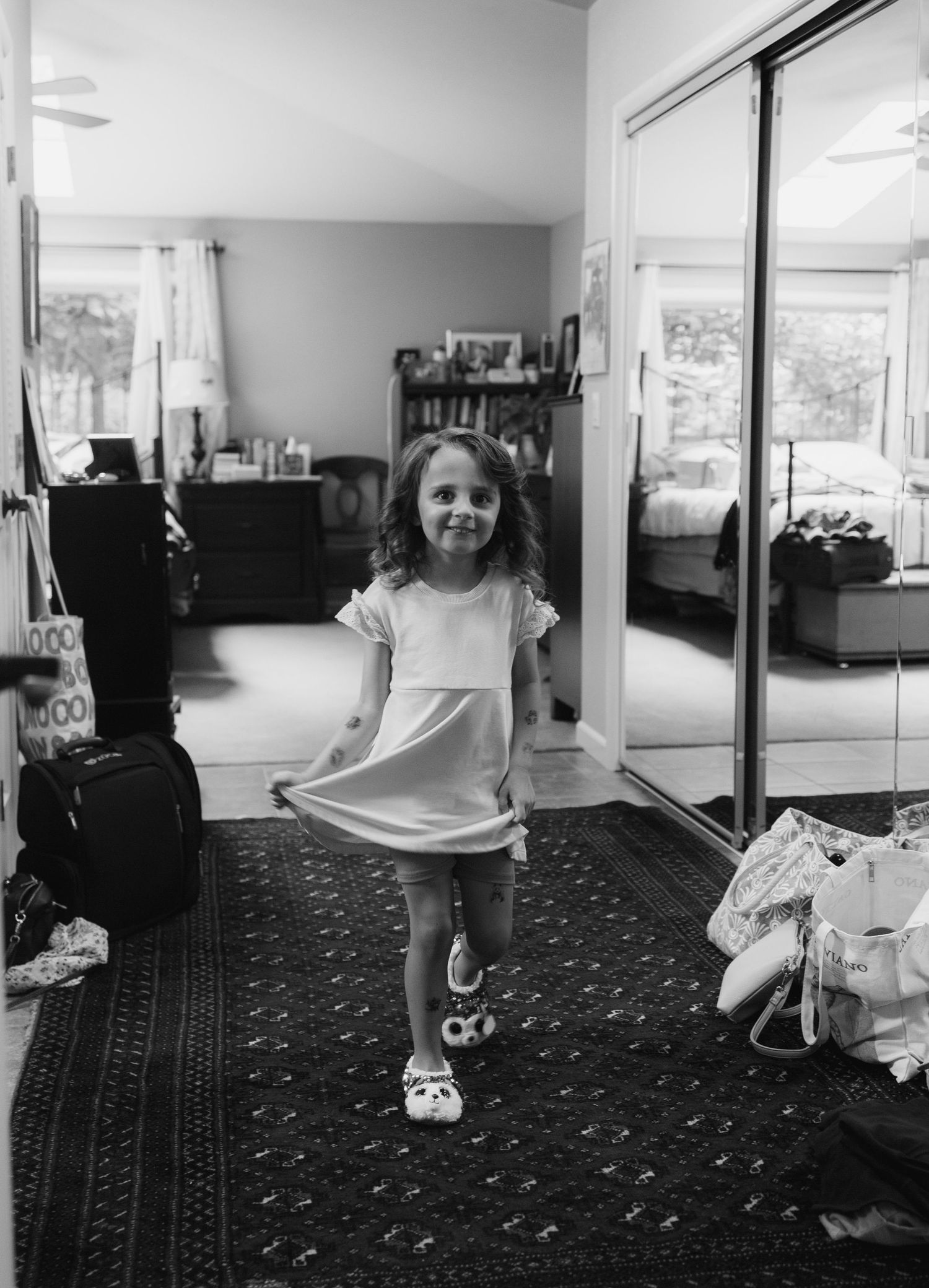 Black and white photo of a young girl in a dress and Crocs twirling in a bedroom with a mirrored closet.