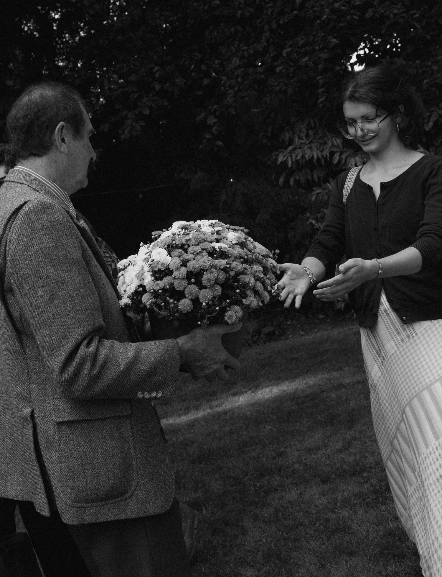 Black and white photo of a man presenting a large bouquet of flowers to a smiling woman wearing glasses outdoors.