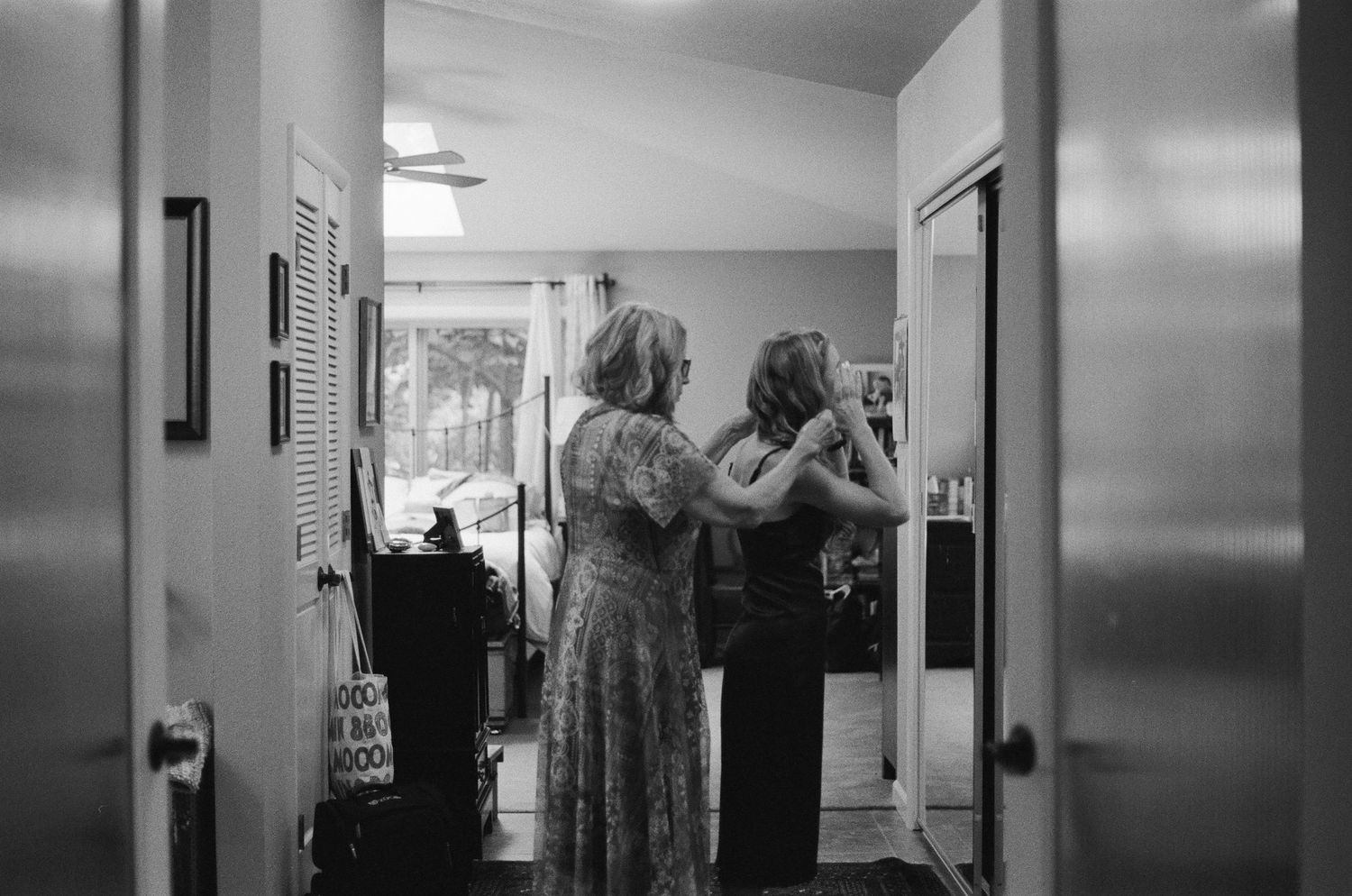 Two women helping each other get ready in a hallway, captured in black and white photography.