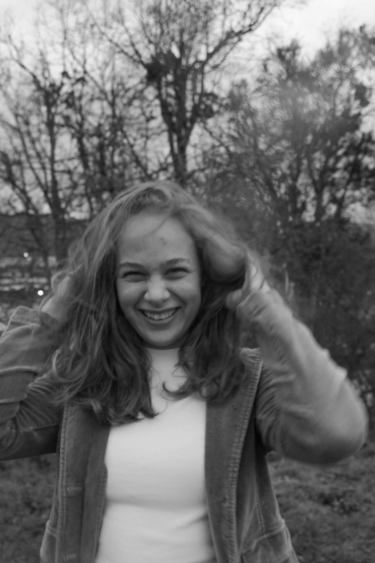Black and white portrait of laughing young woman tossing hair outdoors among bare winter trees.