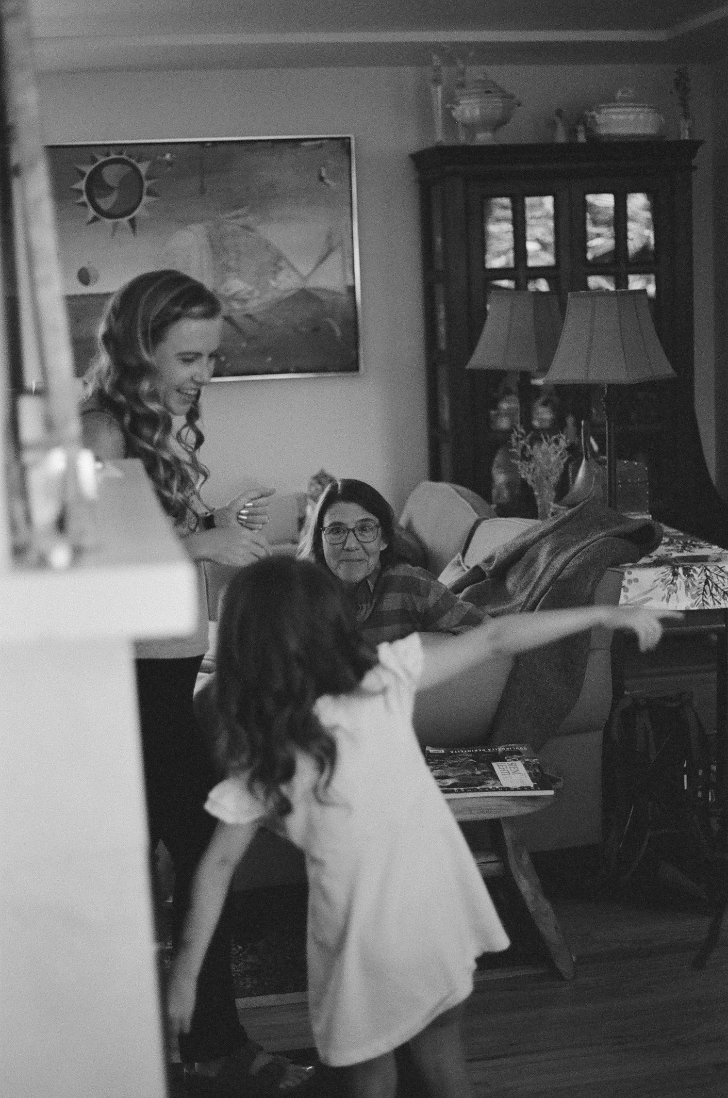 Black and white photo of women and a young girl dancing together in a cozy living room.