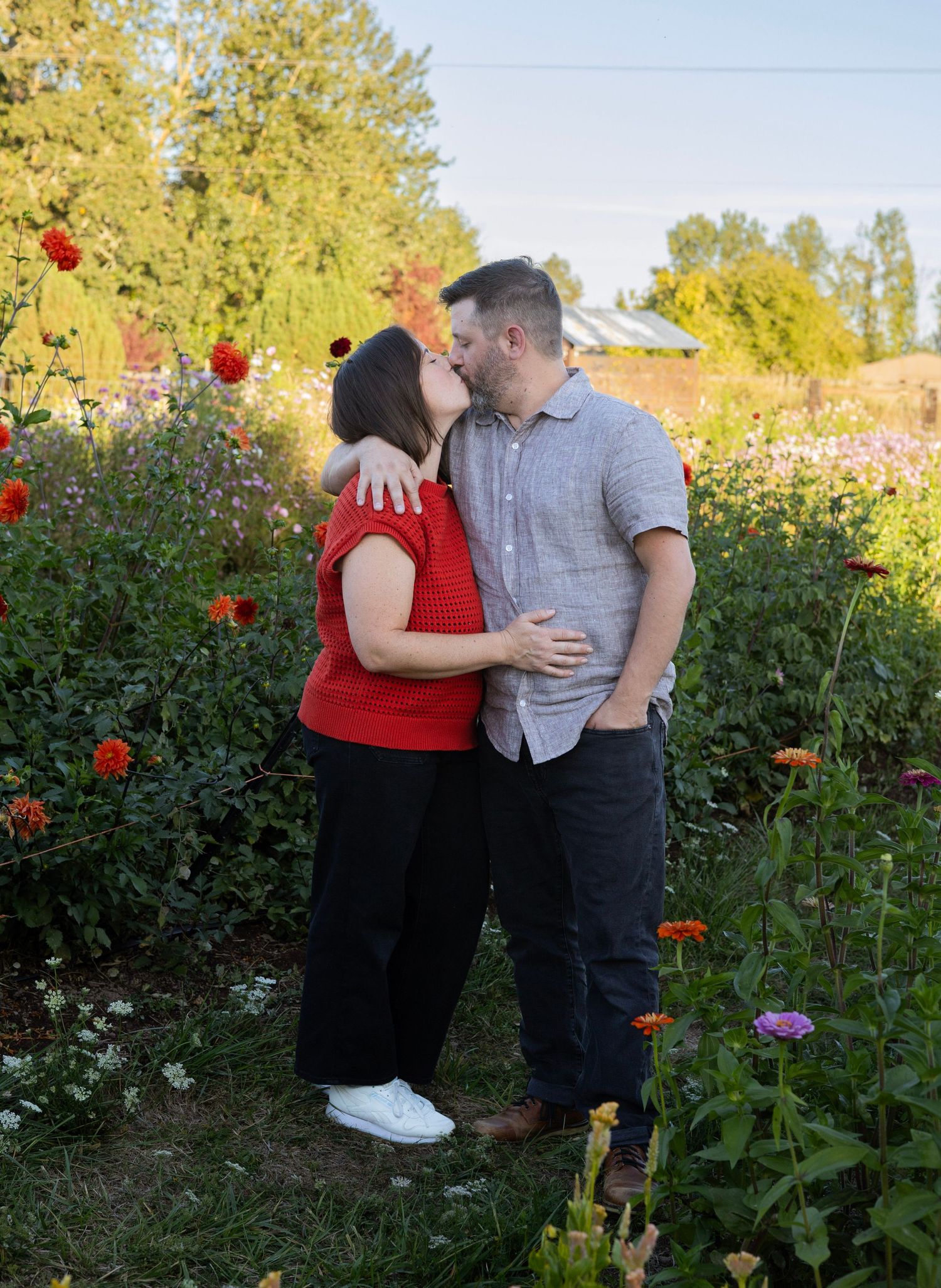 Couple kissing in a colorful flower garden surrounded by dahlias and wildflowers on a sunny day.