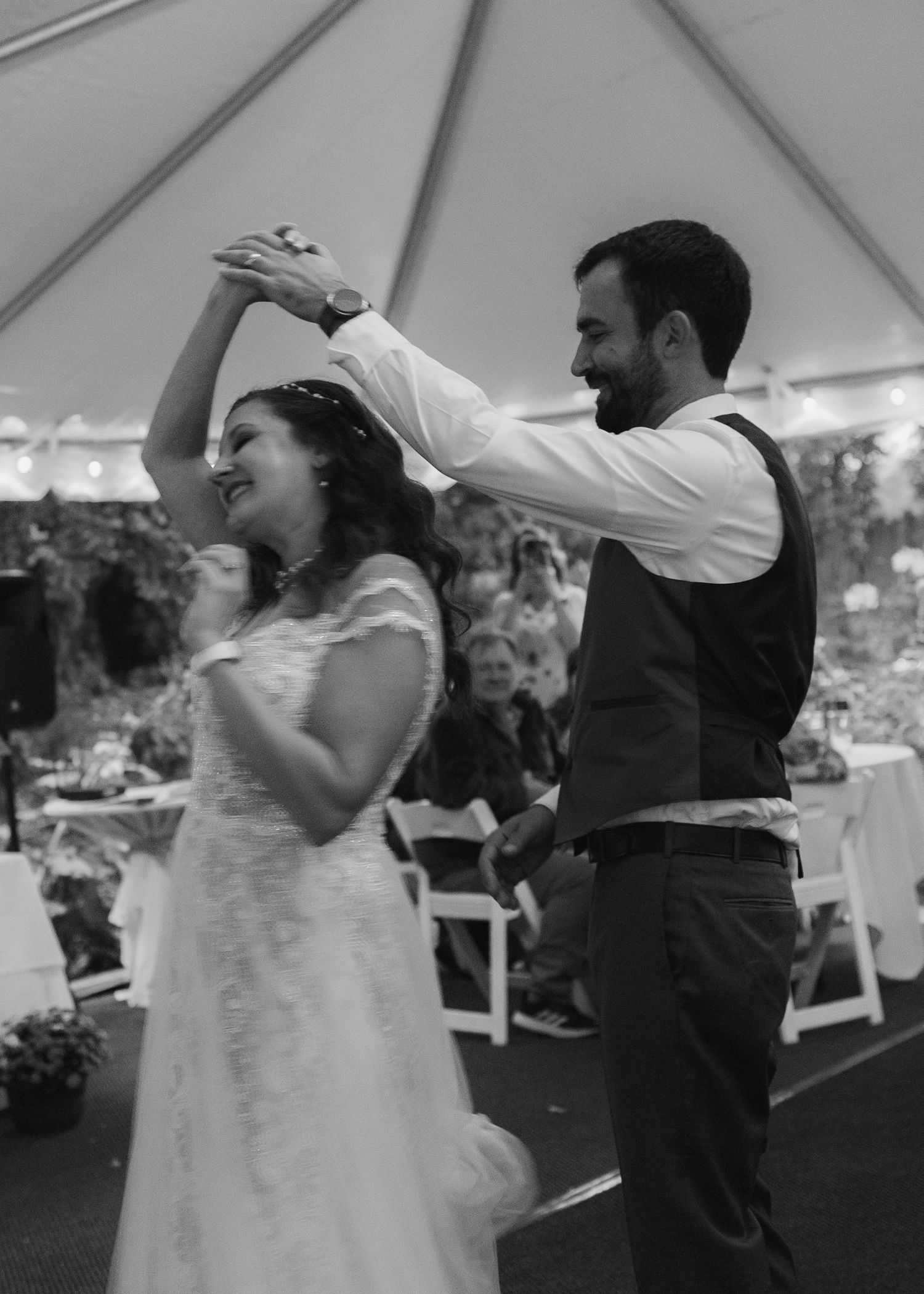 Bride and groom share first dance under wedding tent in black and white photo.