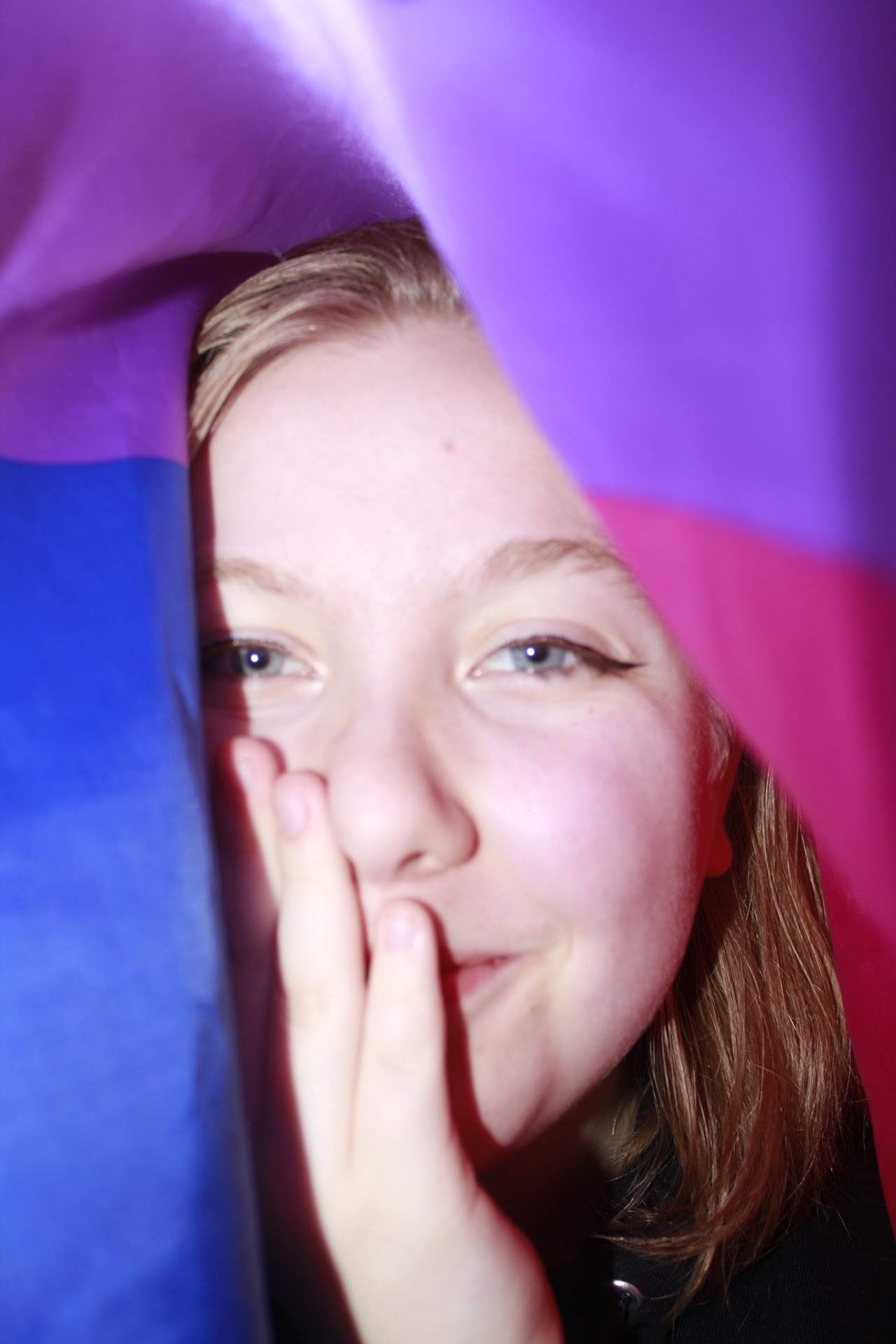 A young girl peeks through colorful purple and blue fabric with a playful expression.