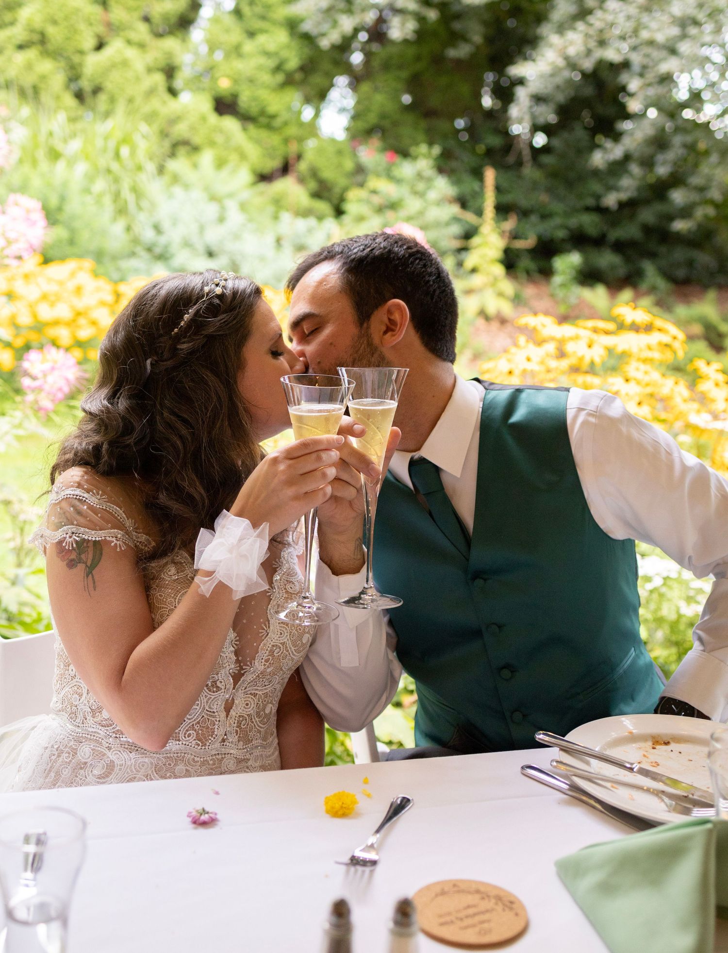 Bride and groom share a kiss while clinking champagne glasses at their outdoor garden wedding reception.