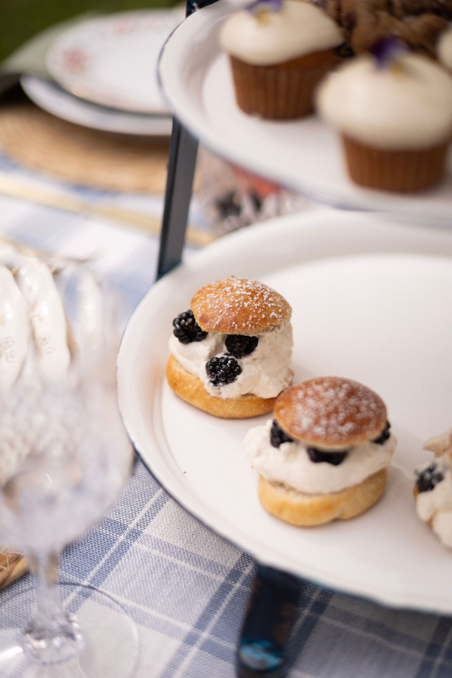 Elegant tiered dessert stand with cream-filled profiteroles topped with blackberries and powdered sugar at an outdoor event.