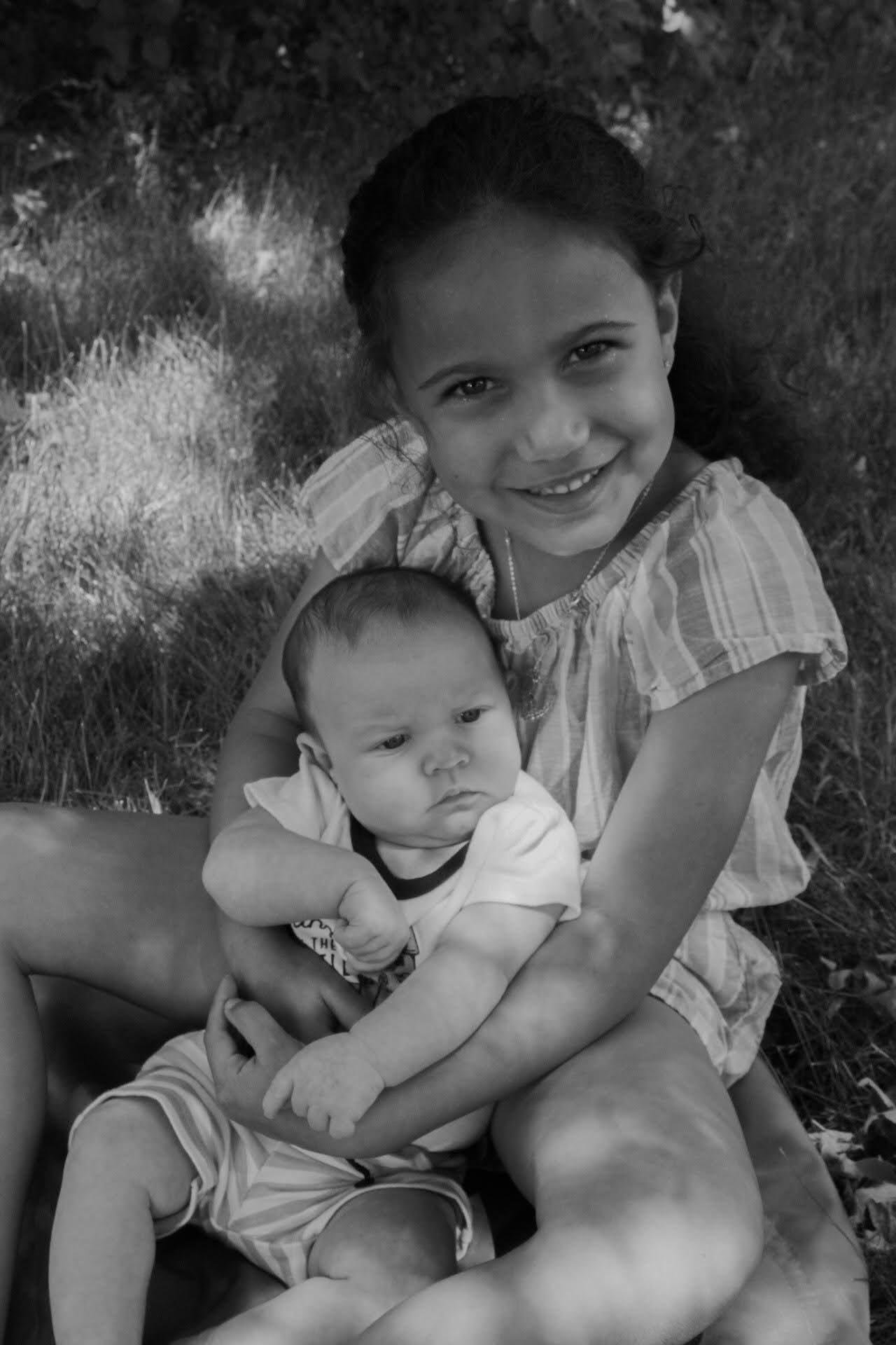 Black and white portrait of a smiling girl holding a newborn baby outdoors.