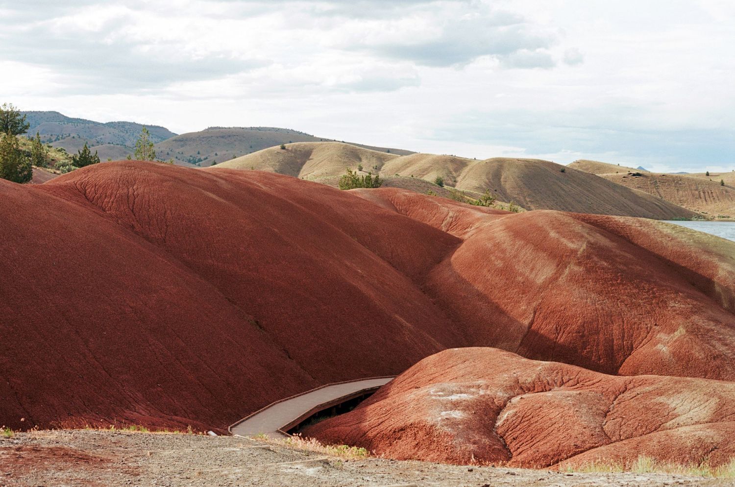 Dramatic red and orange painted hills landscape with winding path under cloudy sky in Oregon.
