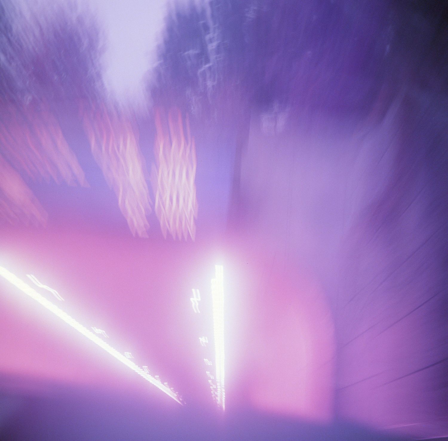 An abstract blurred photograph of purple and white lights creating a dreamy motion effect at night.
