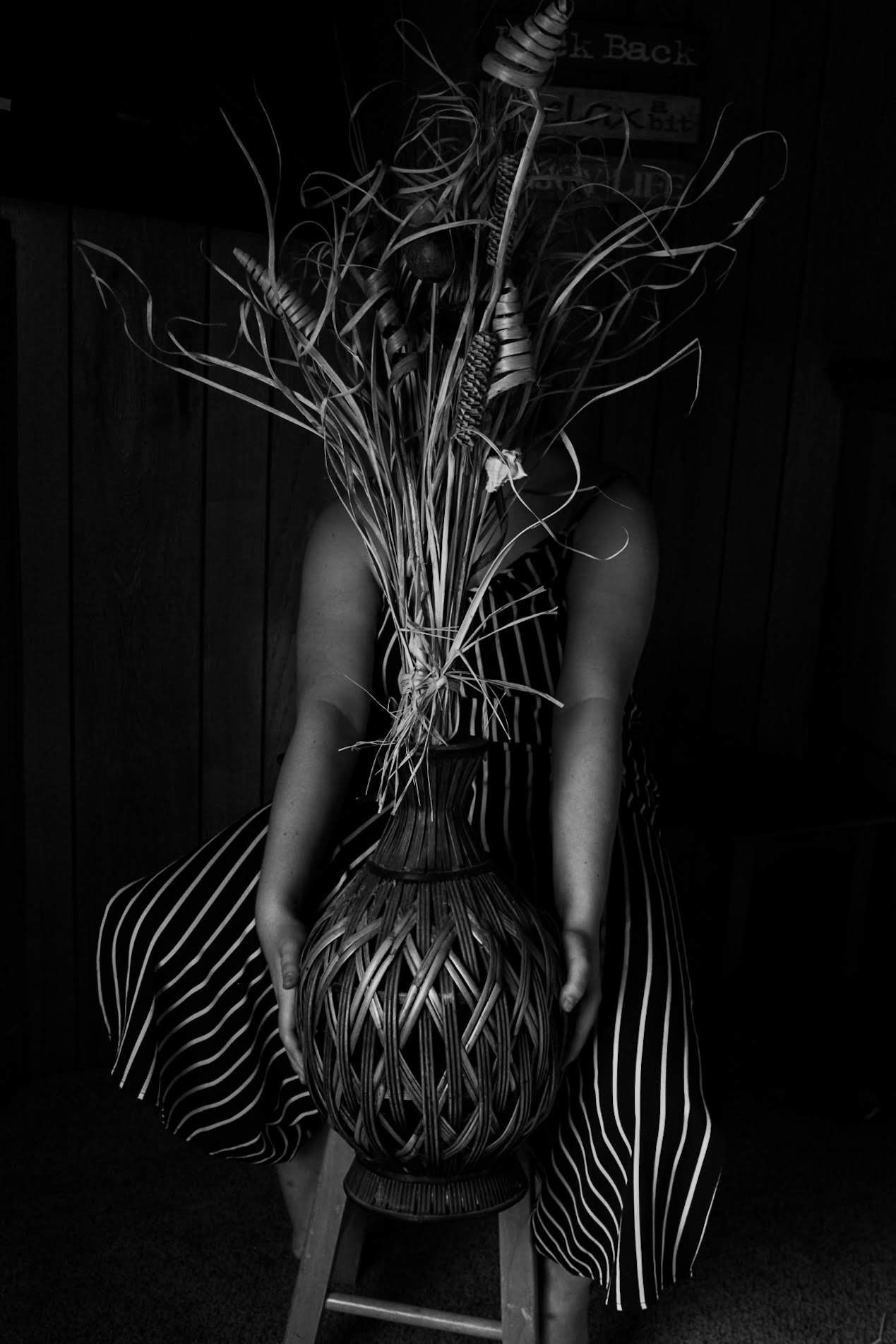 Black and white artistic portrait of a person seated holding a large decorative plant arrangement.