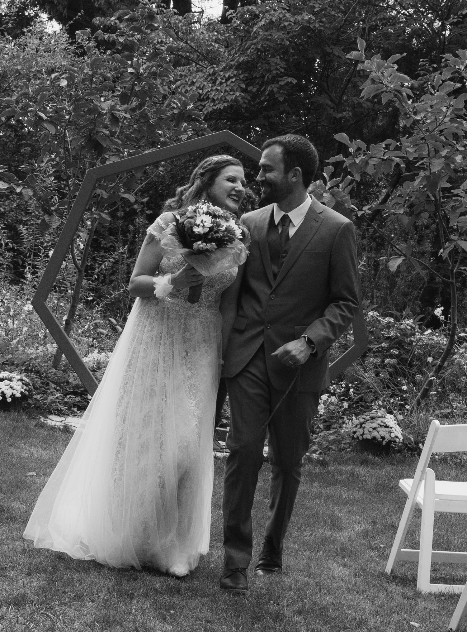 Newlyweds laugh joyfully together in black and white photo near hexagonal wedding arch.