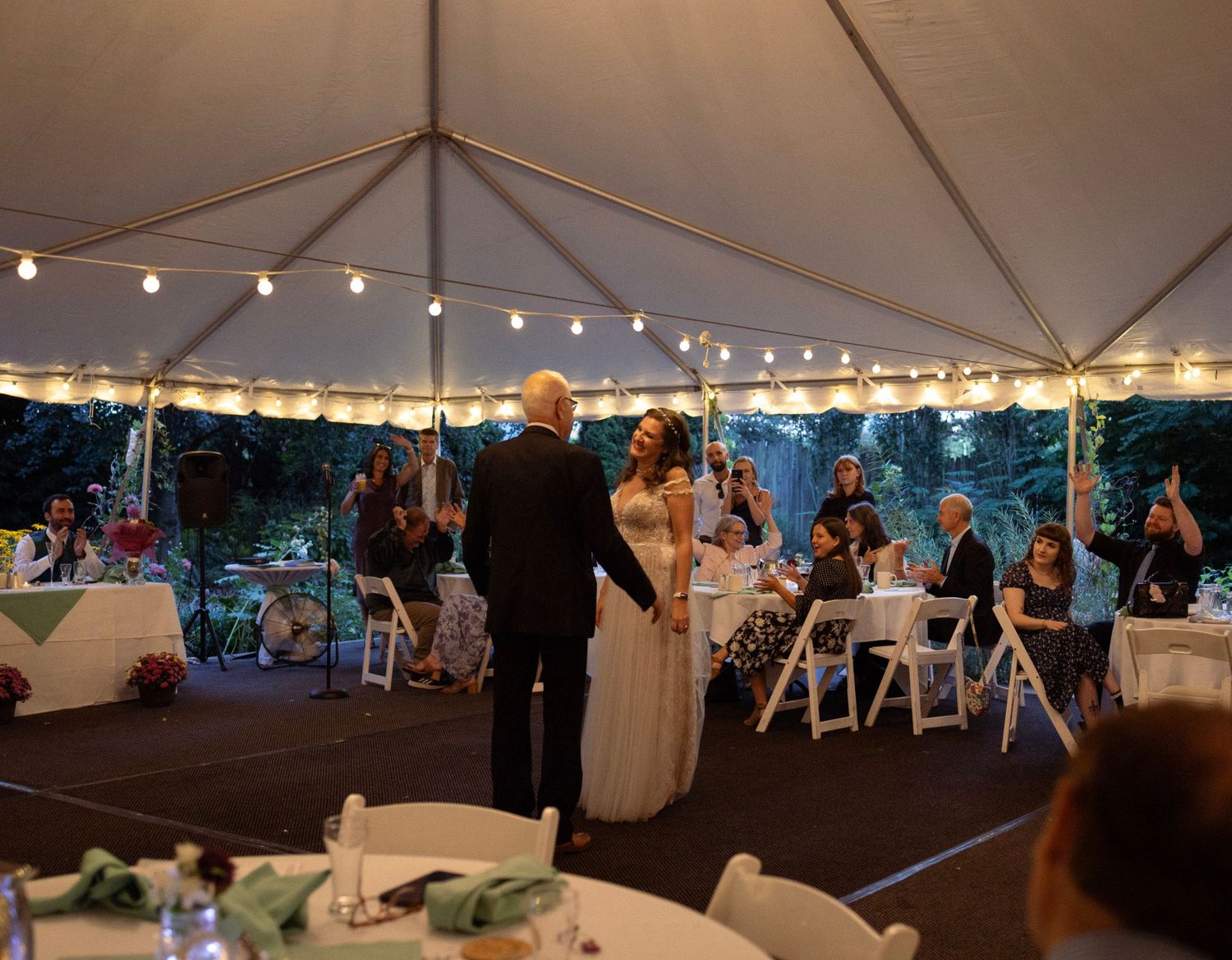 Couple shares romantic first dance under string lights in elegant wedding reception tent.