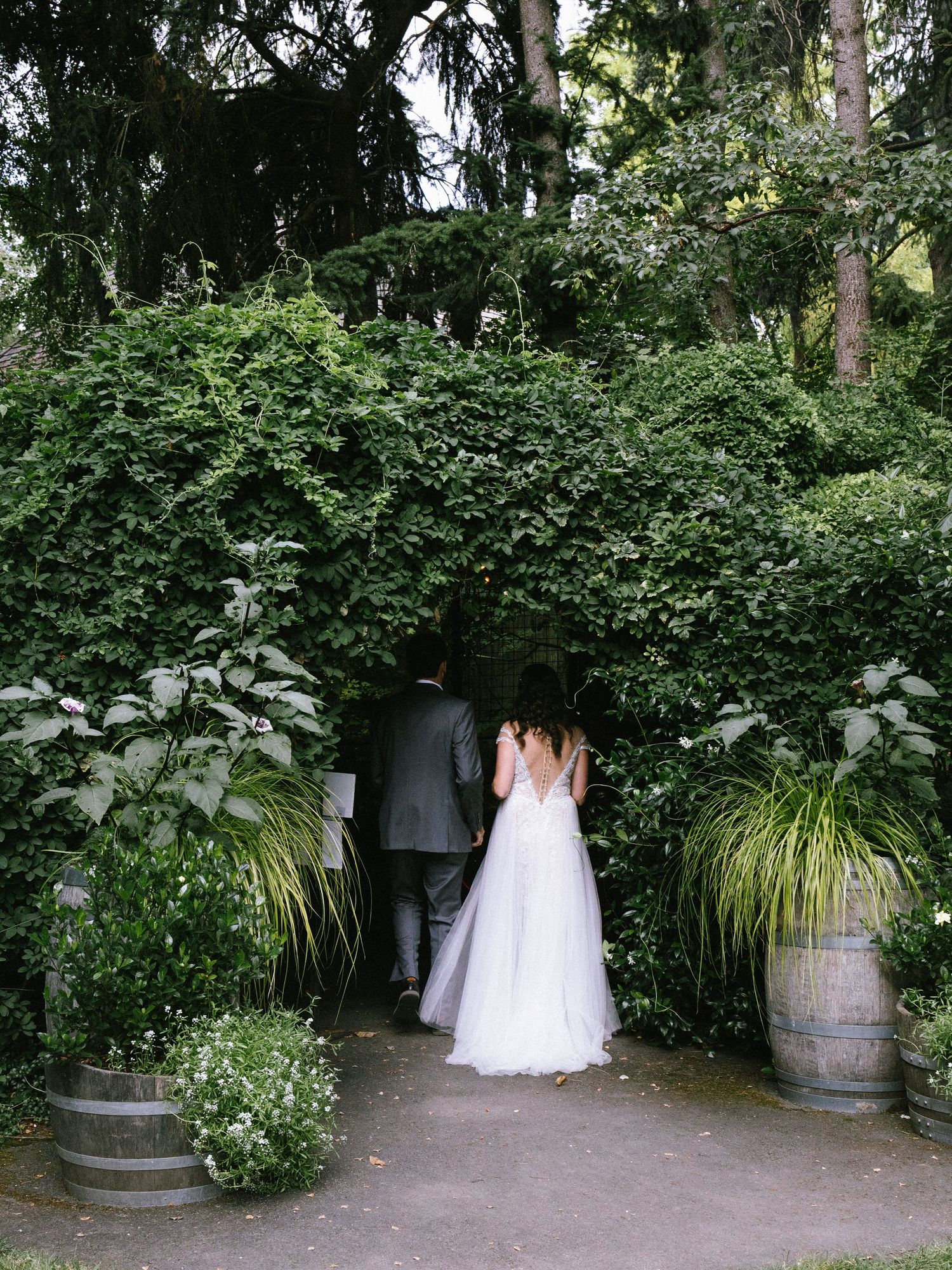 Bride and groom walking through a lush green ivy-covered garden archway at an outdoor wedding venue.