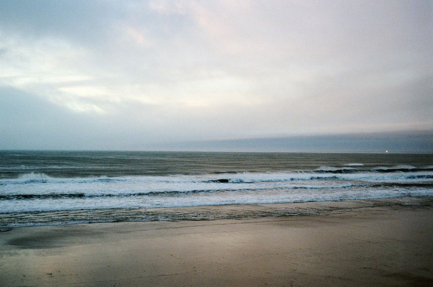 Calm ocean beach scene with gentle waves under an overcast sky captured on film photography.