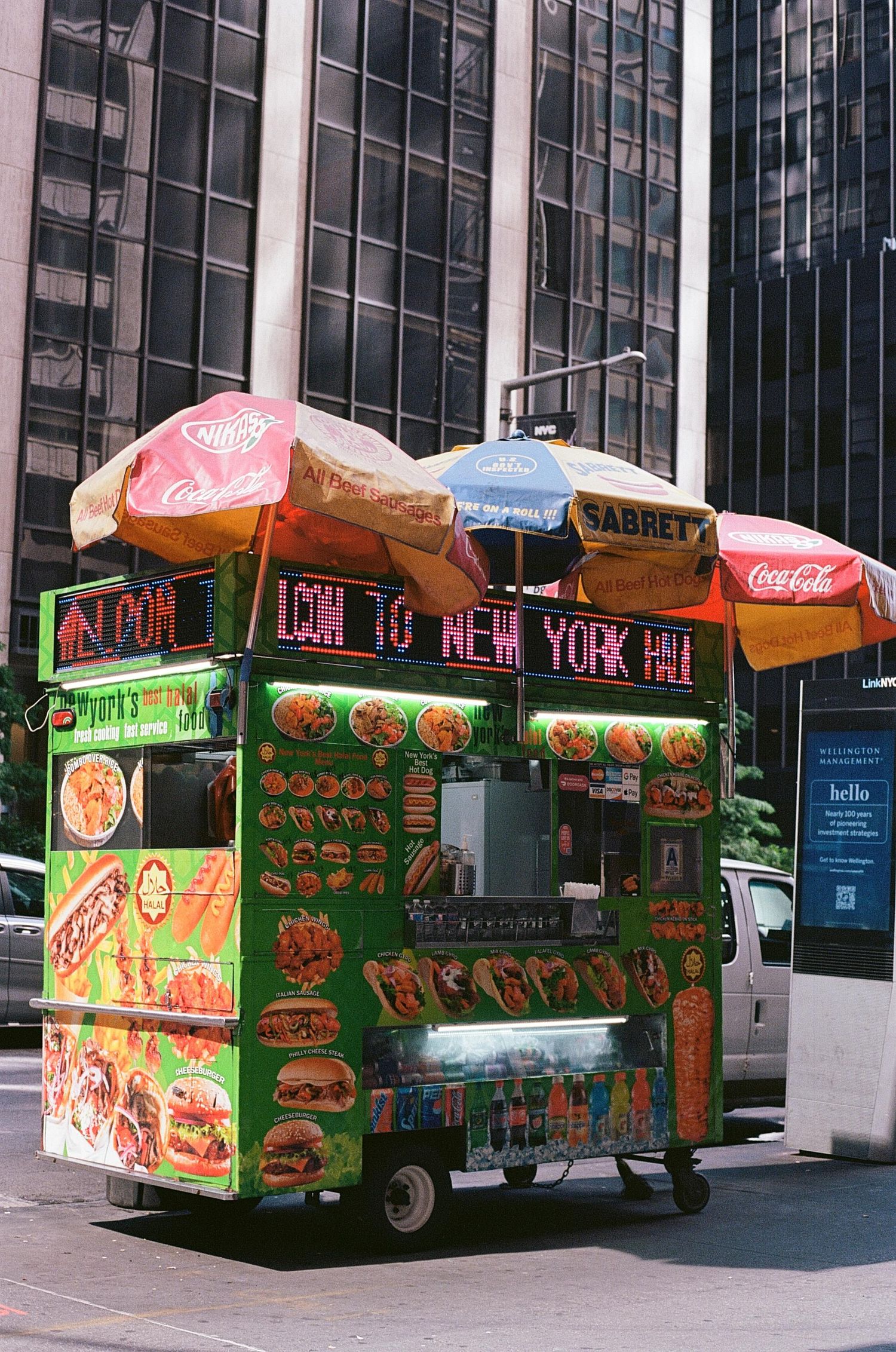 A colorful Sabrett hot dog street food cart with umbrellas and neon signs on a busy New York City street.