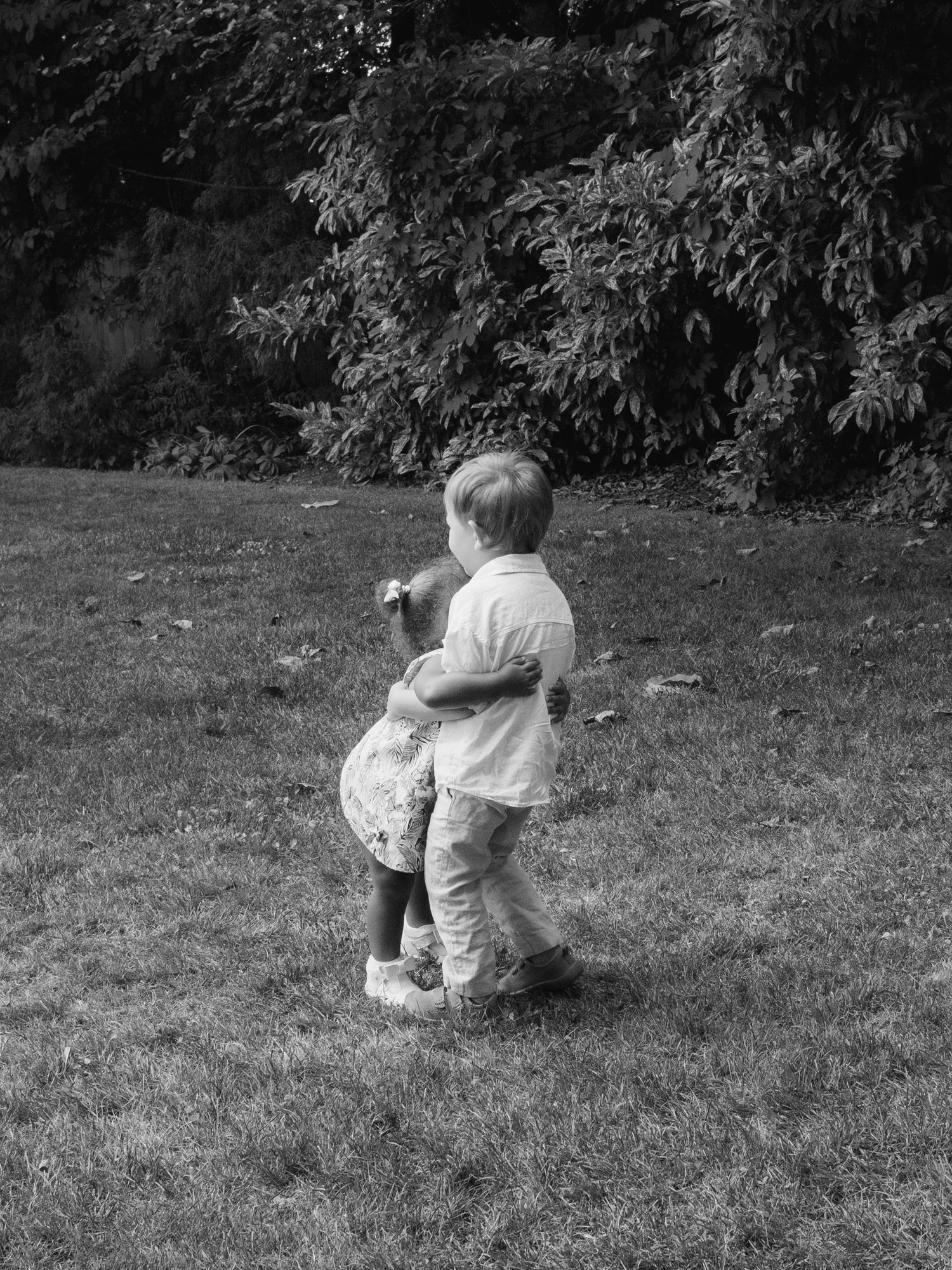 Two young children hug each other on green lawn in black and white photo.