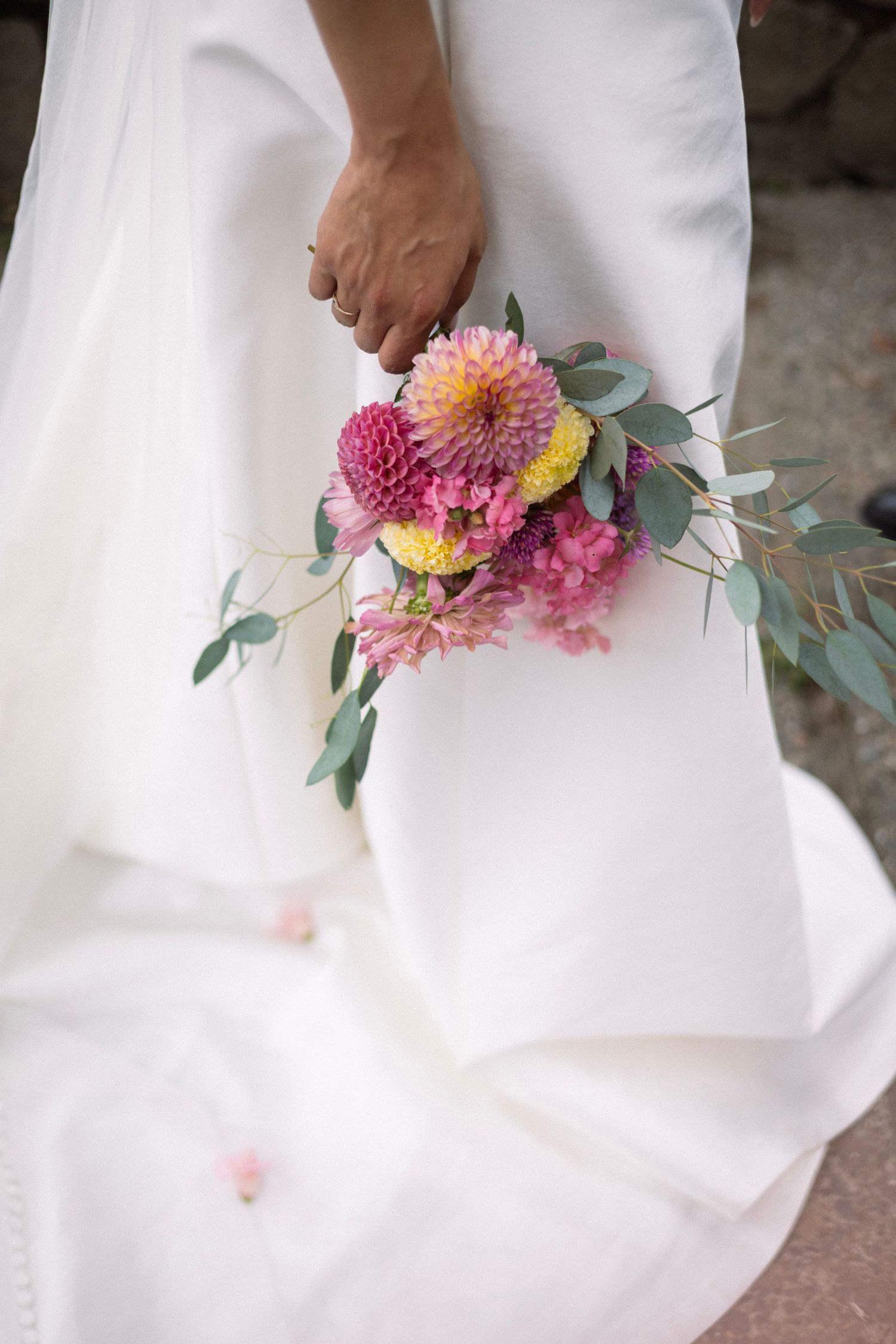 Bride in white gown holding a vibrant pink and yellow dahlia wedding bouquet with eucalyptus greenery.