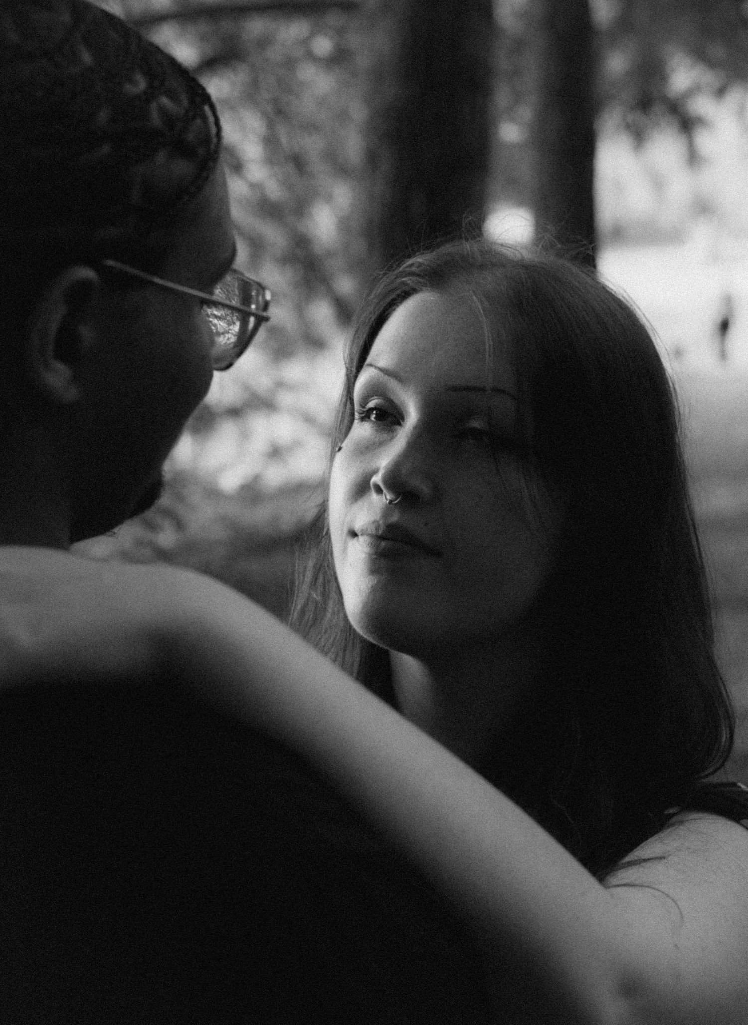 Black and white close-up of a woman gazing up at her partner outdoors, capturing an intimate romantic moment.
