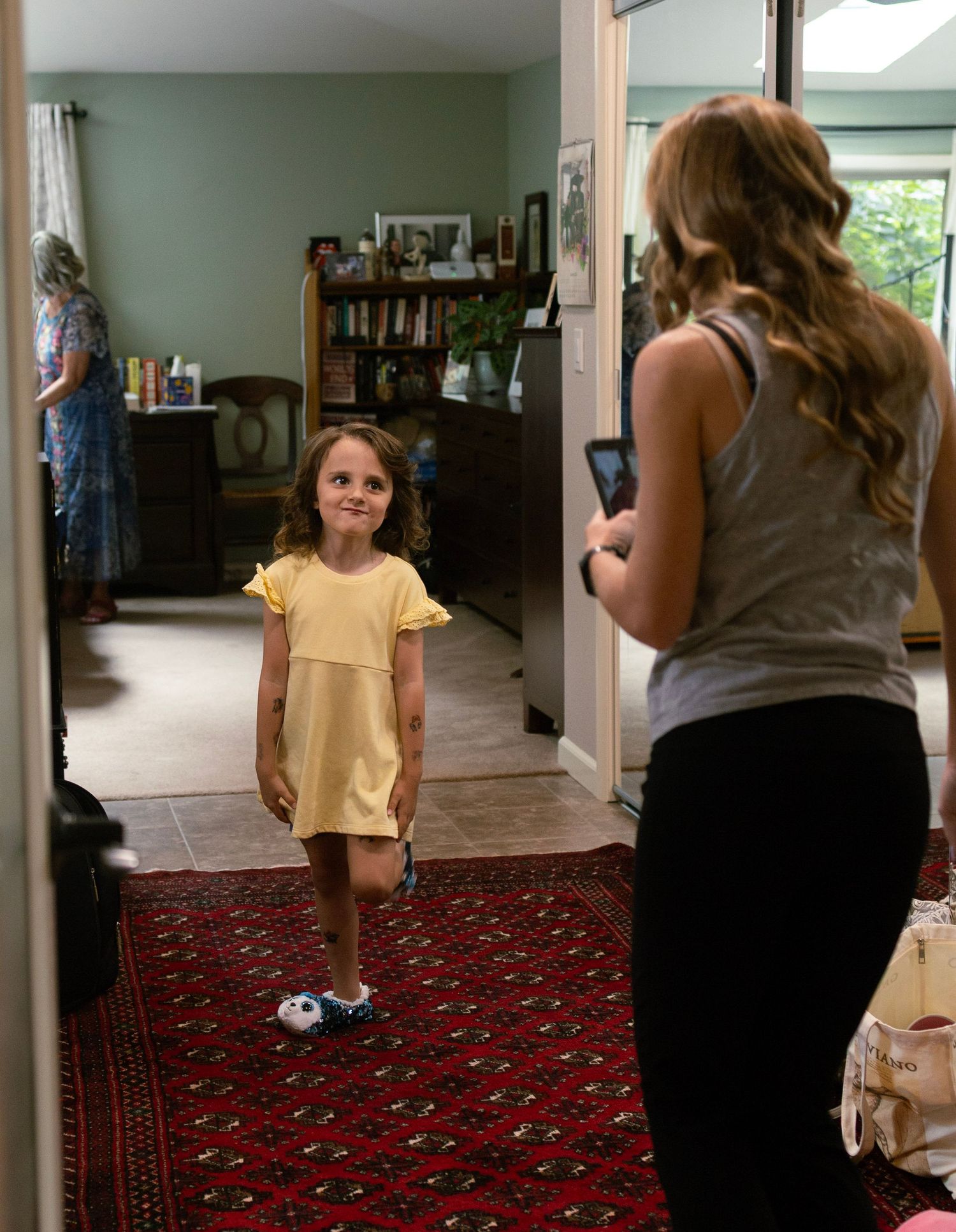 A young girl in a yellow dress stands in a hallway while a woman photographs her before a wedding.