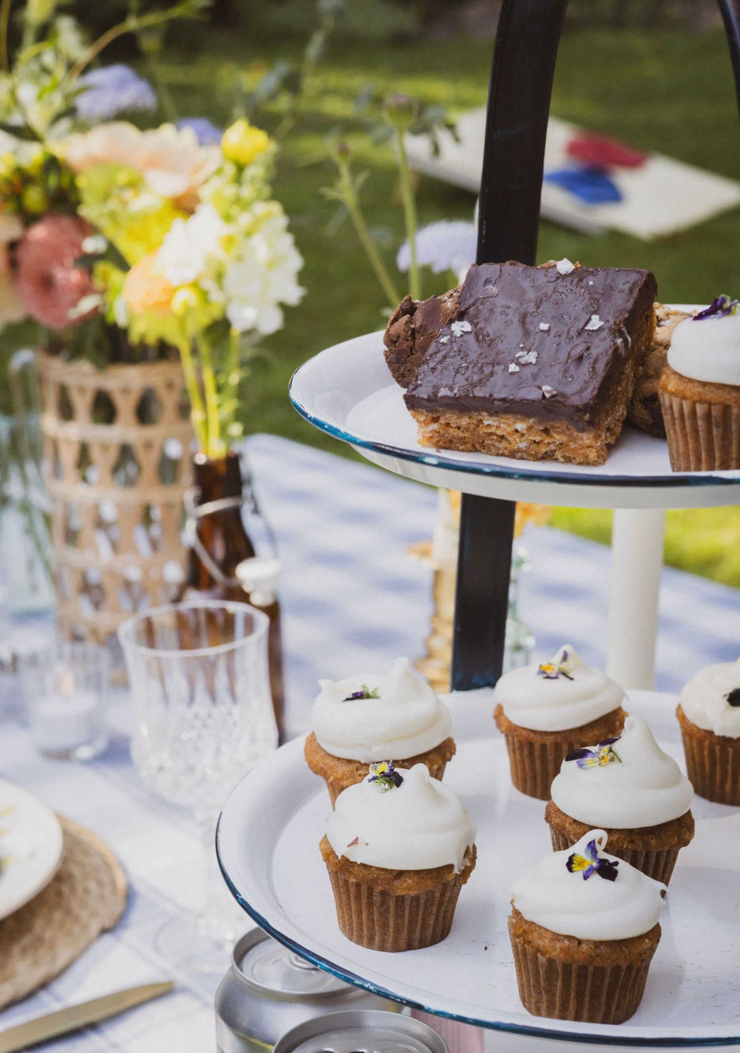 Two-tier dessert stand with white-frosted cupcakes and chocolate brownies at an outdoor garden party.