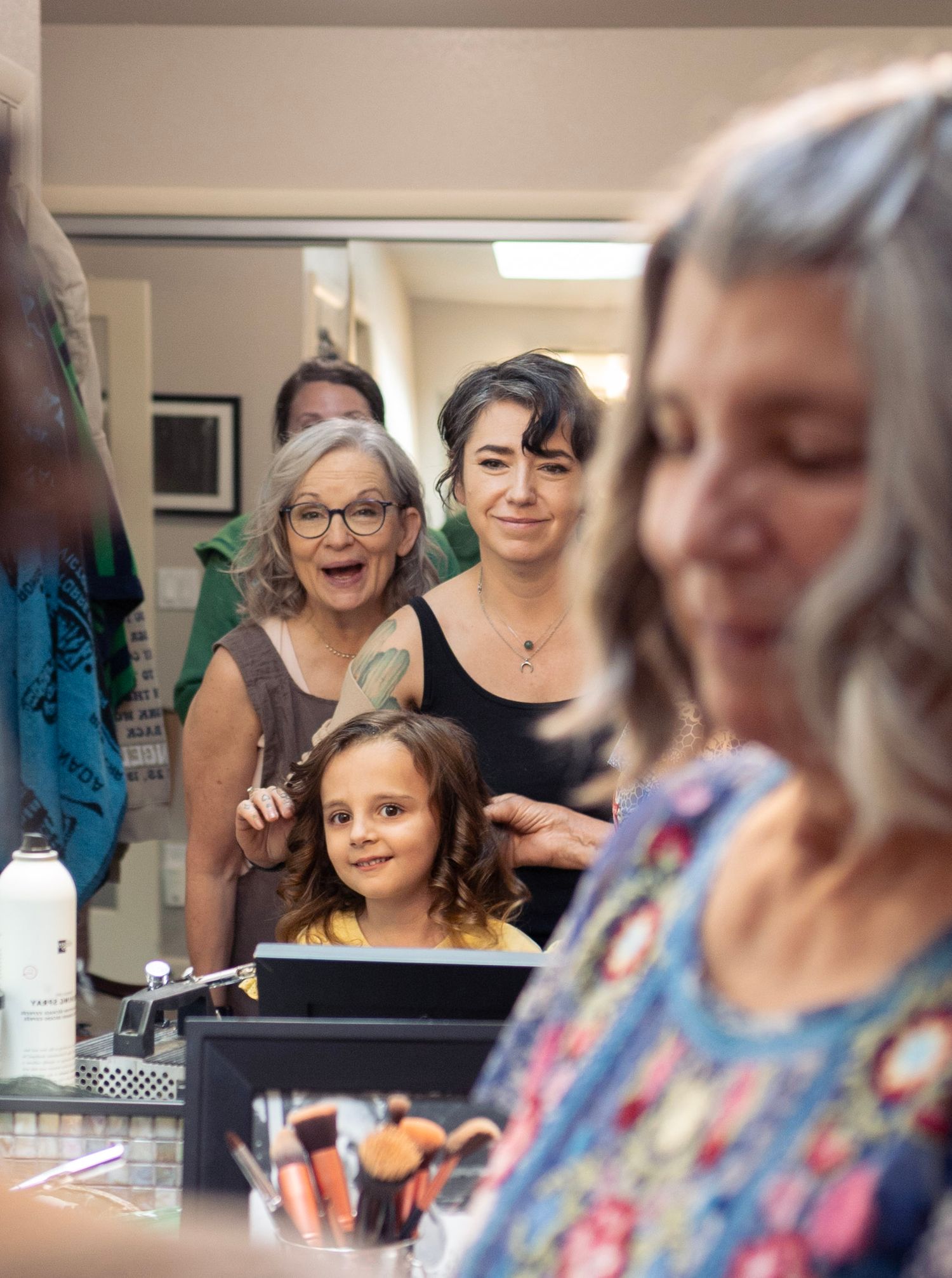 Excited women and a young girl getting ready together in a mirror reflection during bridal preparations.