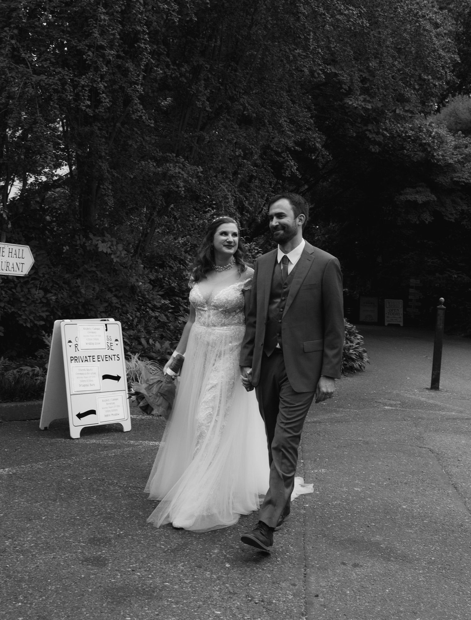 Black and white photo of a bride and groom walking hand in hand outside a venue with a private events sign.