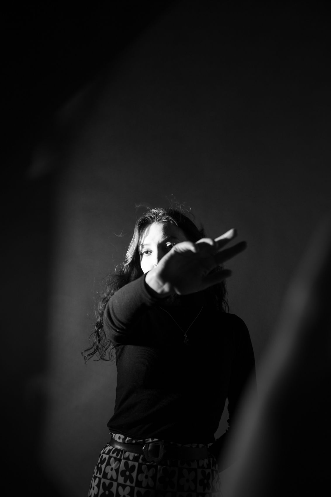 Black and white dramatic portrait of a woman with long hair pointing toward camera in studio lighting.