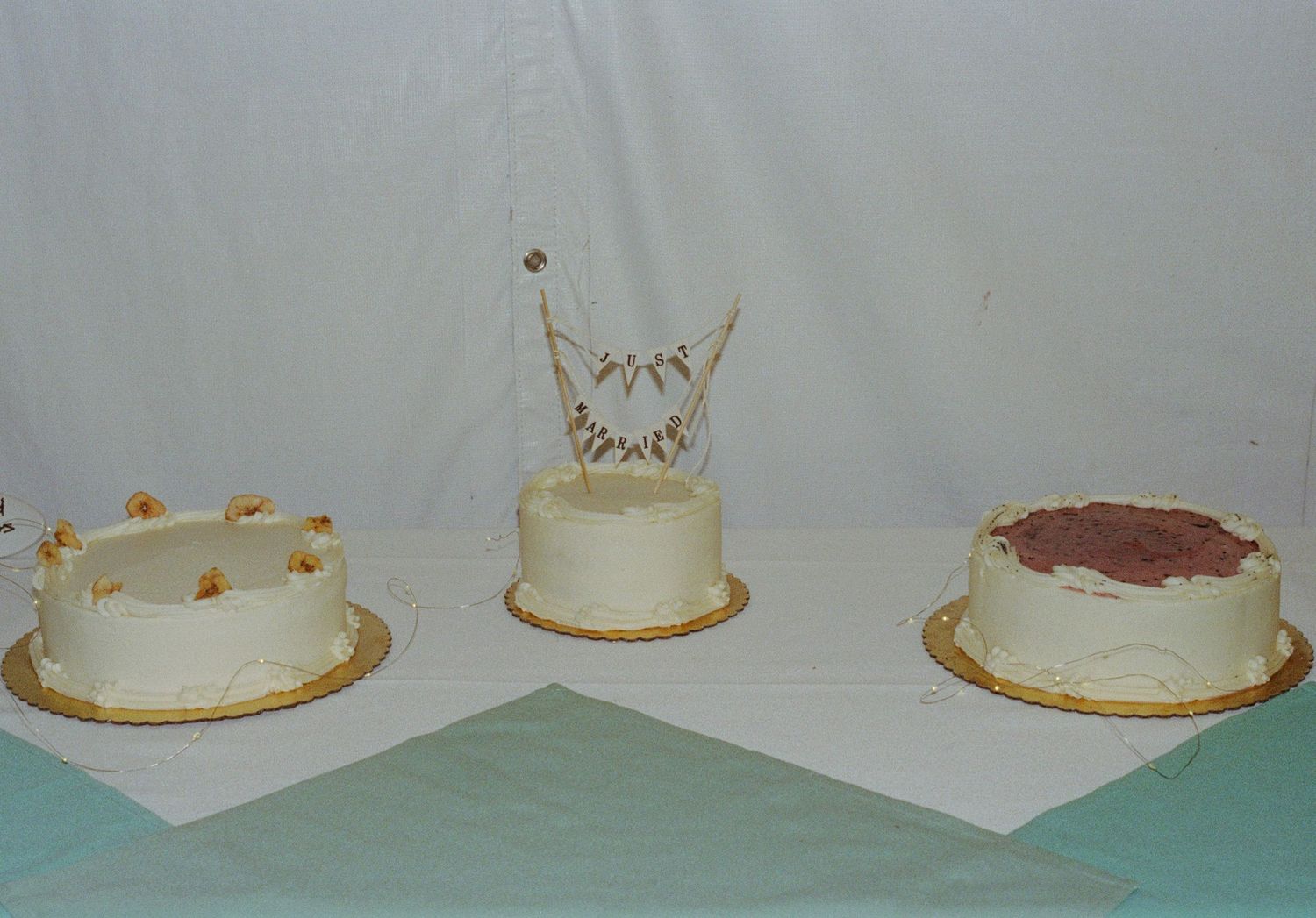 Three white frosted celebration cakes displayed on a table, including a wedding cake with decorative topper.