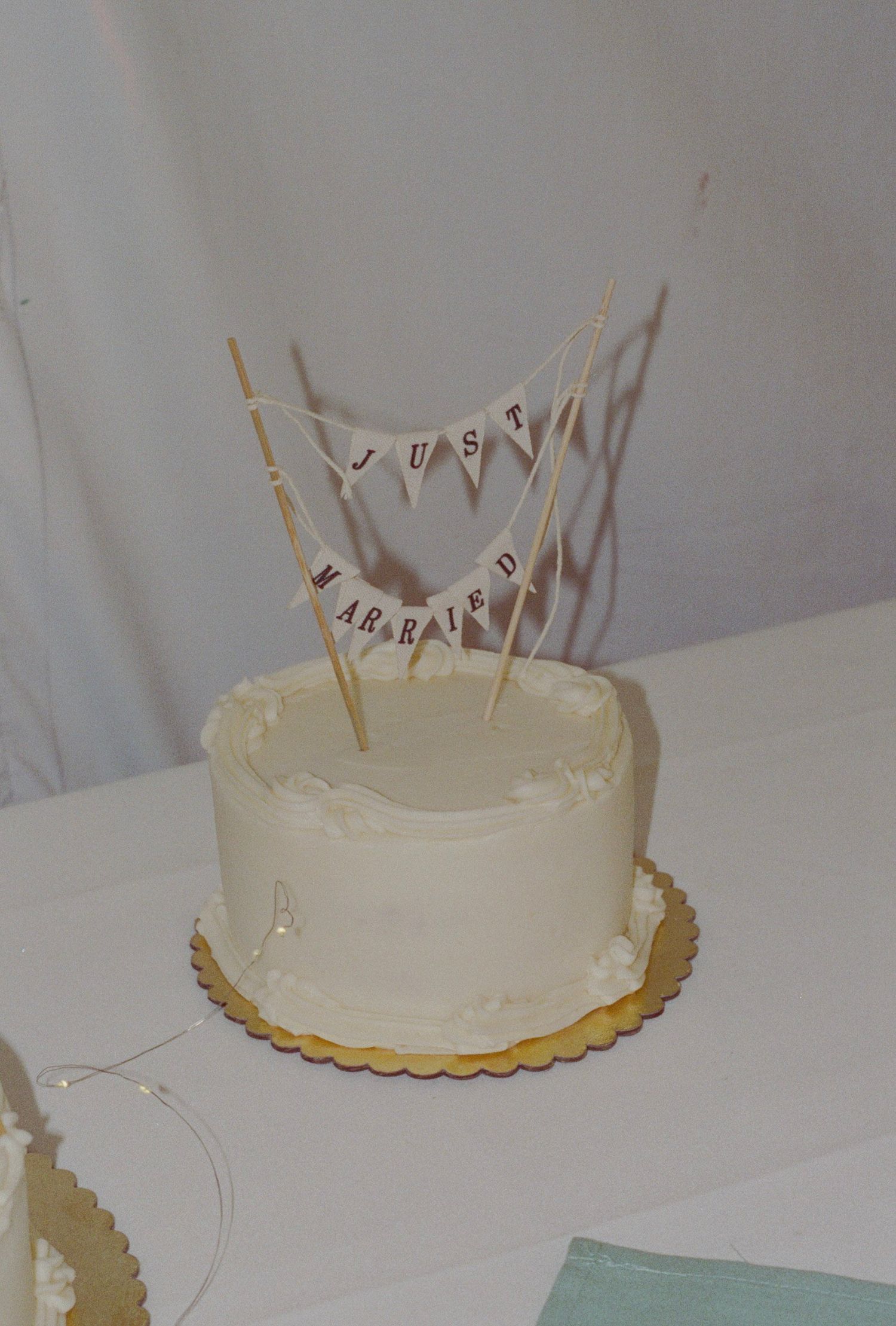 White single-tier wedding cake with Just Married bunting topper on gold cake board.