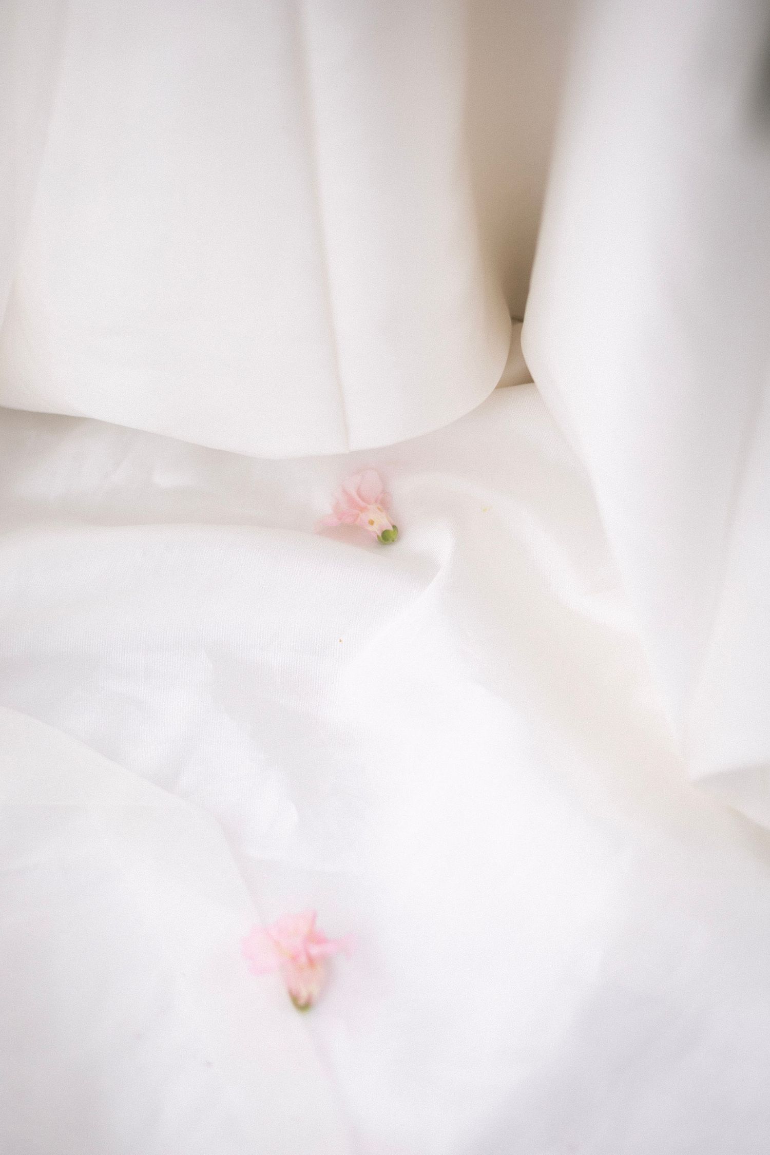 Close-up of delicate pink flower buds scattered on soft white wedding dress fabric.
