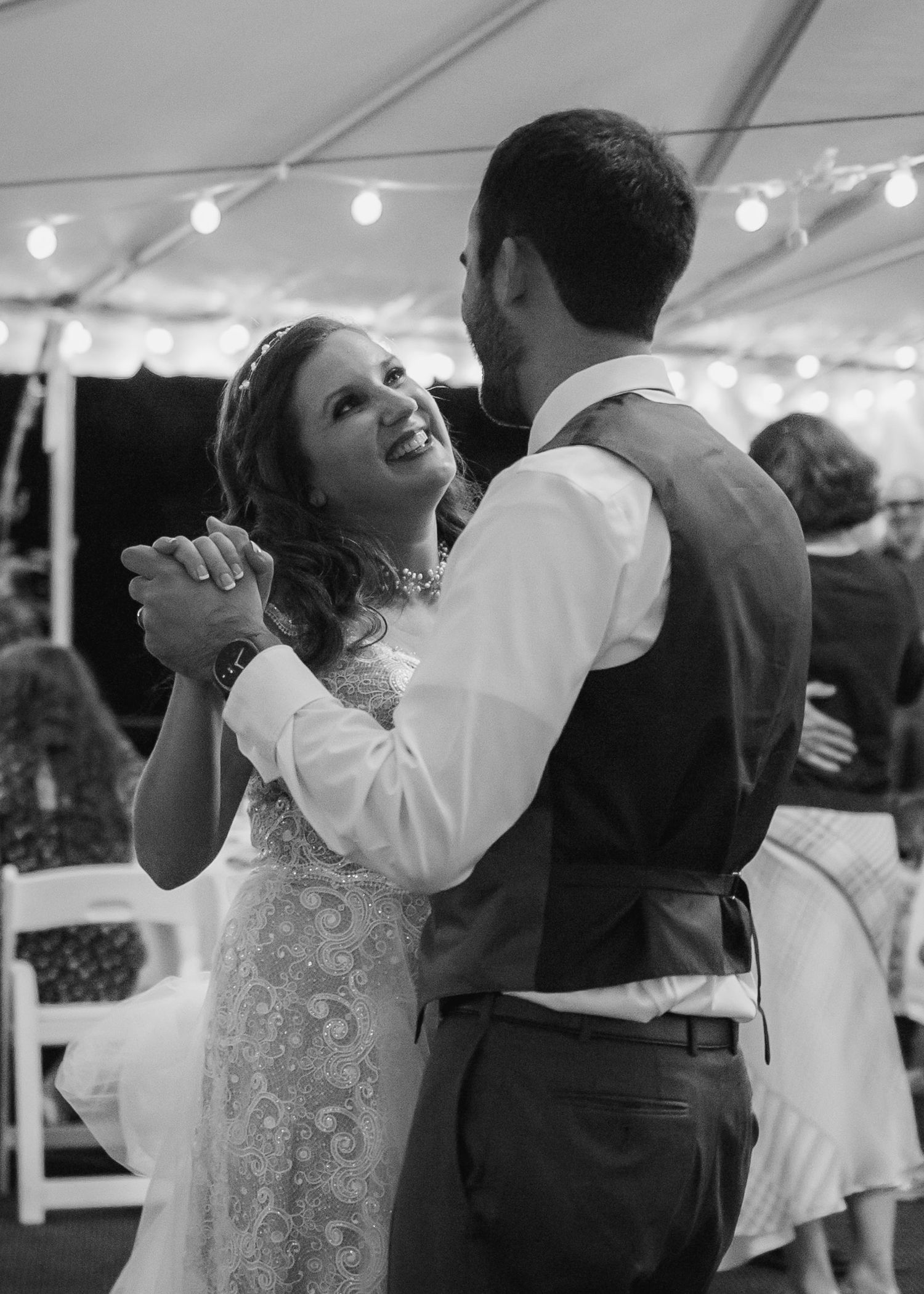 Bride and groom share first dance under string lights in black and white wedding reception photo.