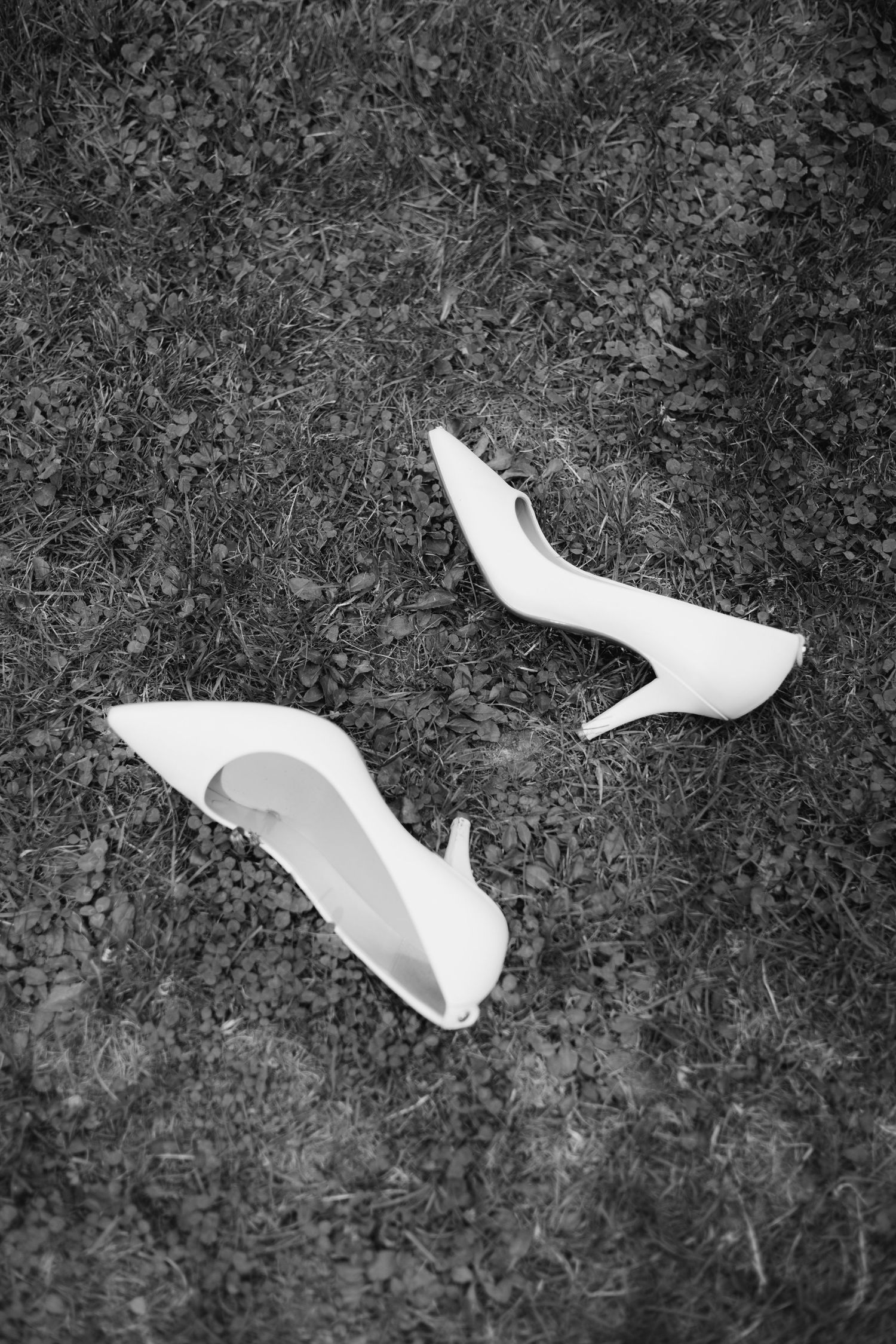 Black and white photo of white bridal high heel shoes resting on grass.