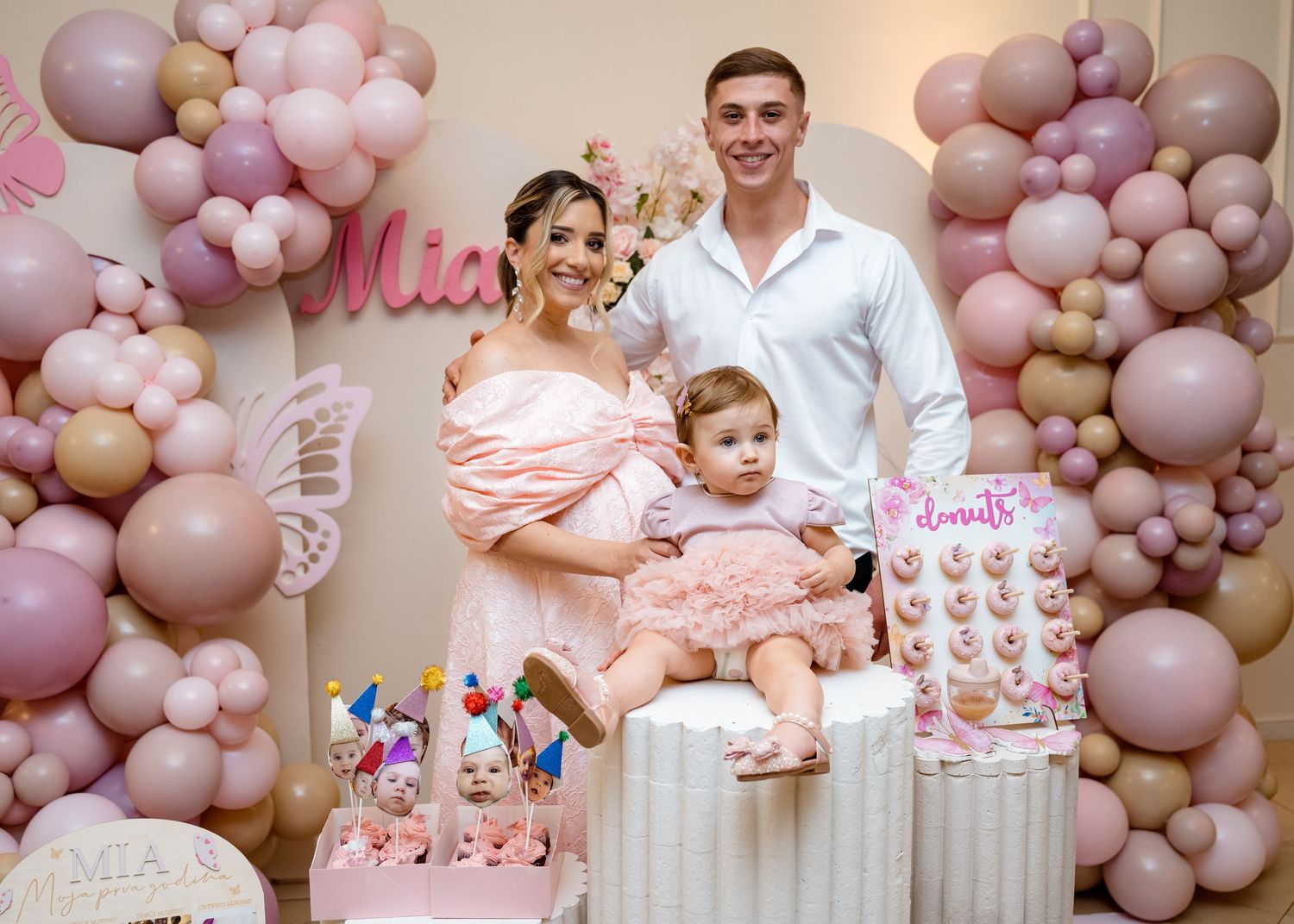 Family portrait of parents and baby girl at Mia's pink first birthday party.