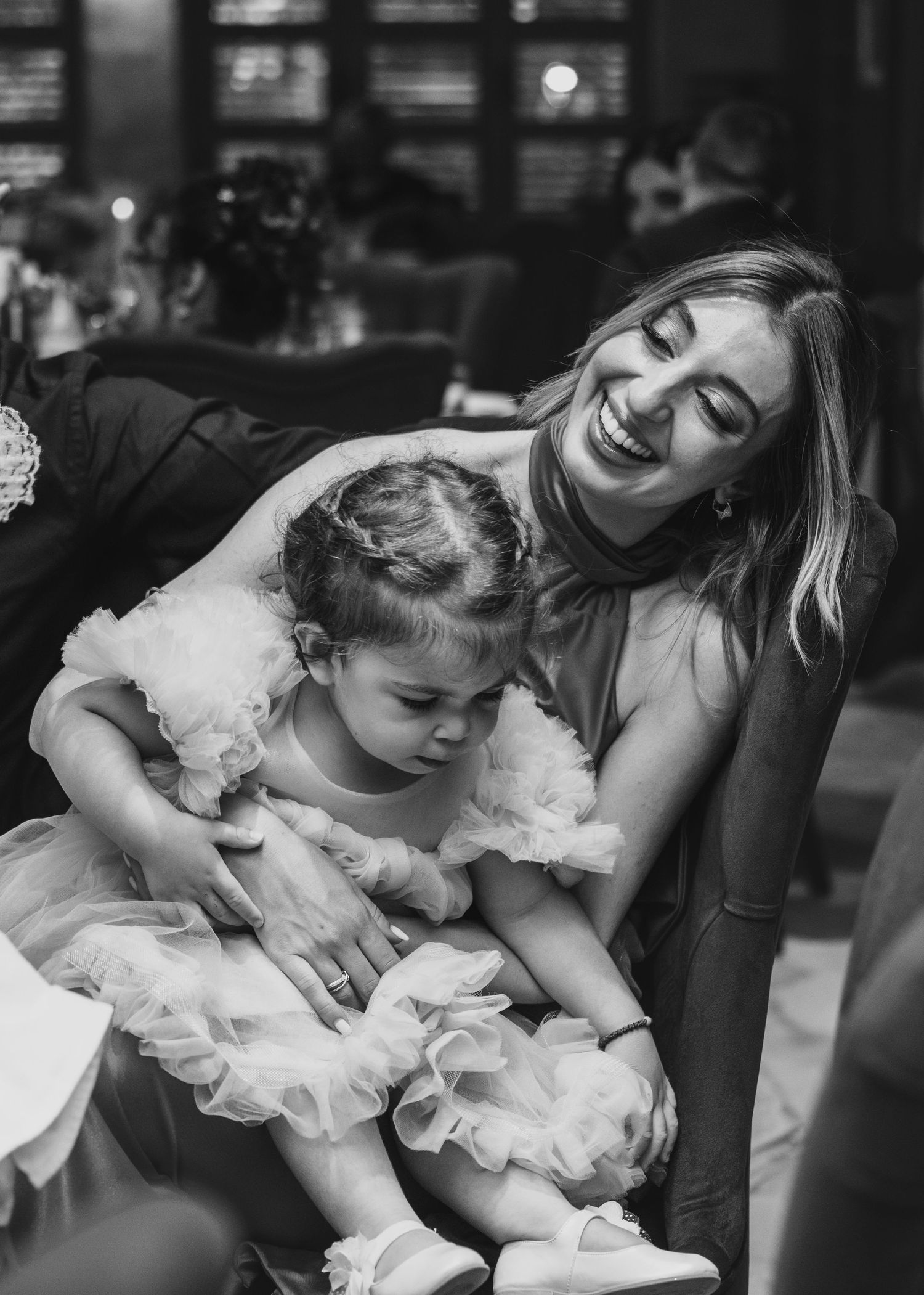 Joyful woman laughing with adorable toddler in tulle dress at wedding.