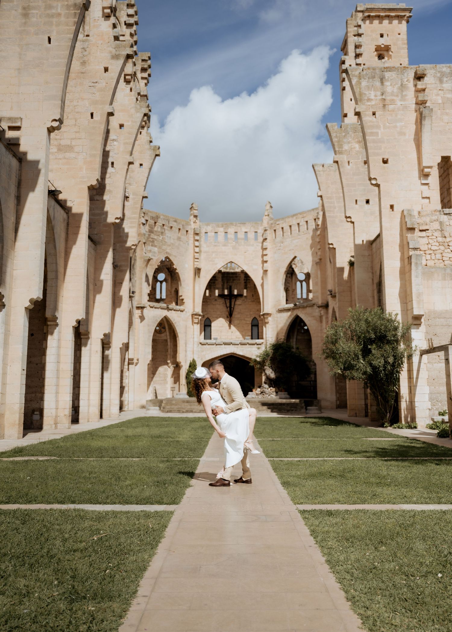 Groom lifts bride in romantic dip along garden path of stunning ancient stone ruins.