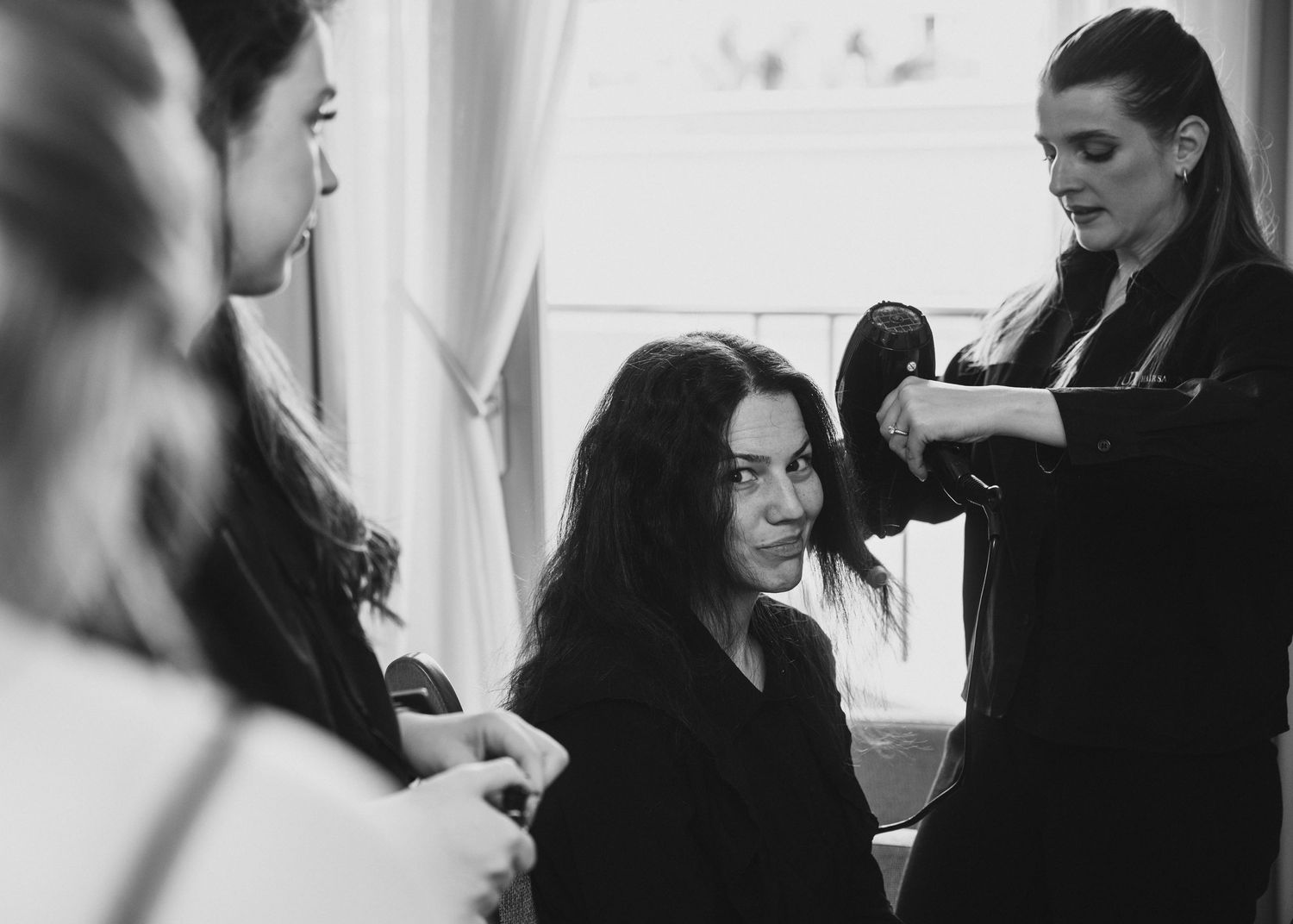 Hairstylist blow-drying dark-haired woman's hair in black and white bridal preparation photo.