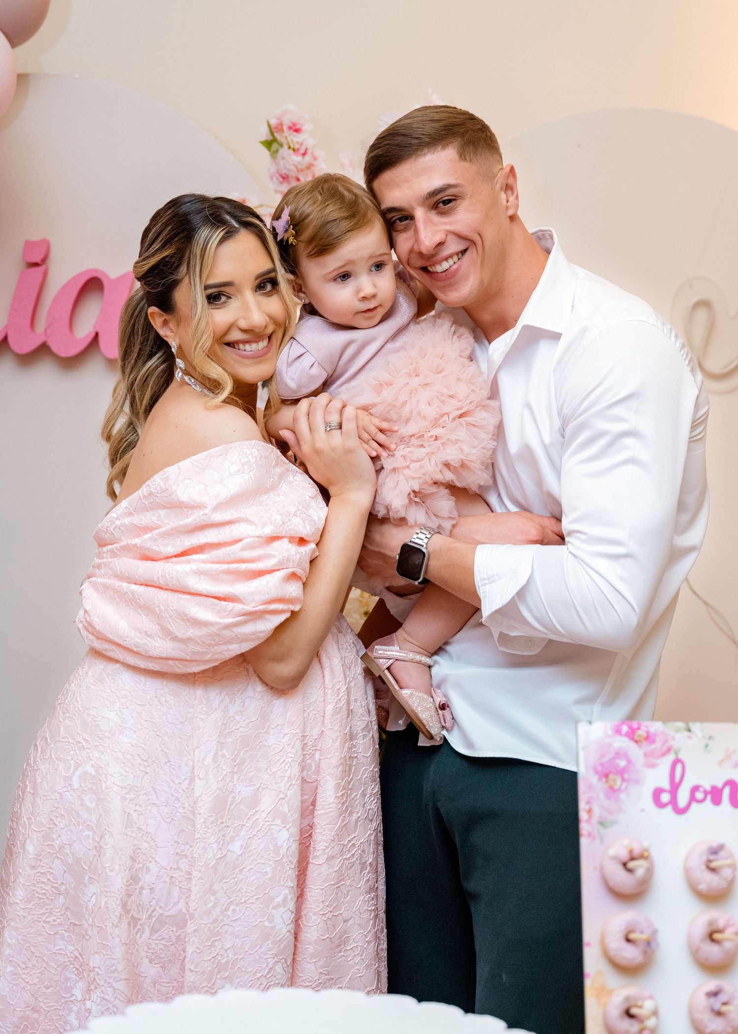 Happy family with baby girl in pink dress celebrating her first birthday party.