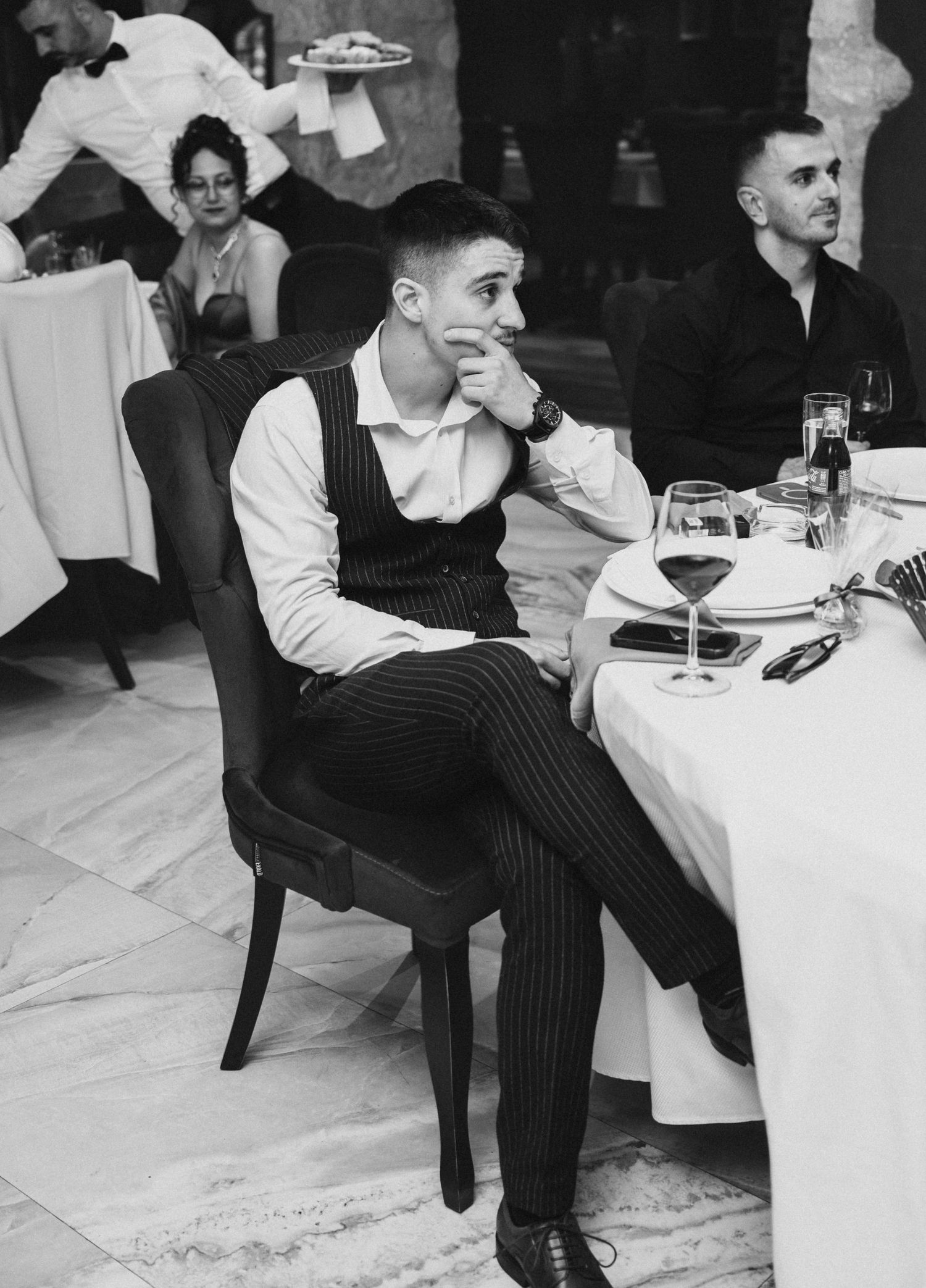 Young man in vest sitting pensively at elegant wedding reception table.