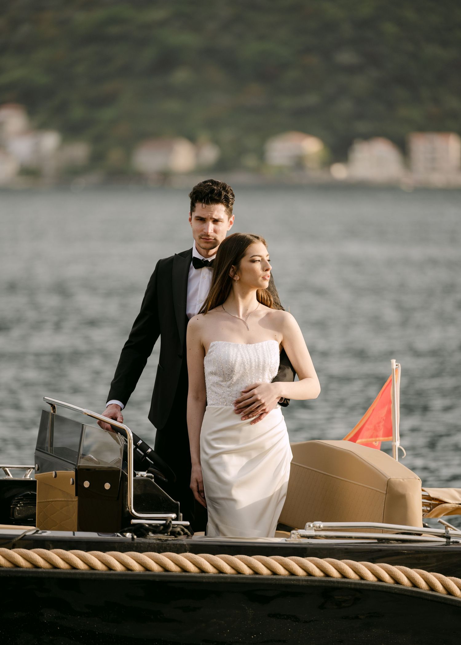 Groom in tuxedo embracing bride in strapless gown on a luxury boat on the Bay of Kotor, Montenegro.