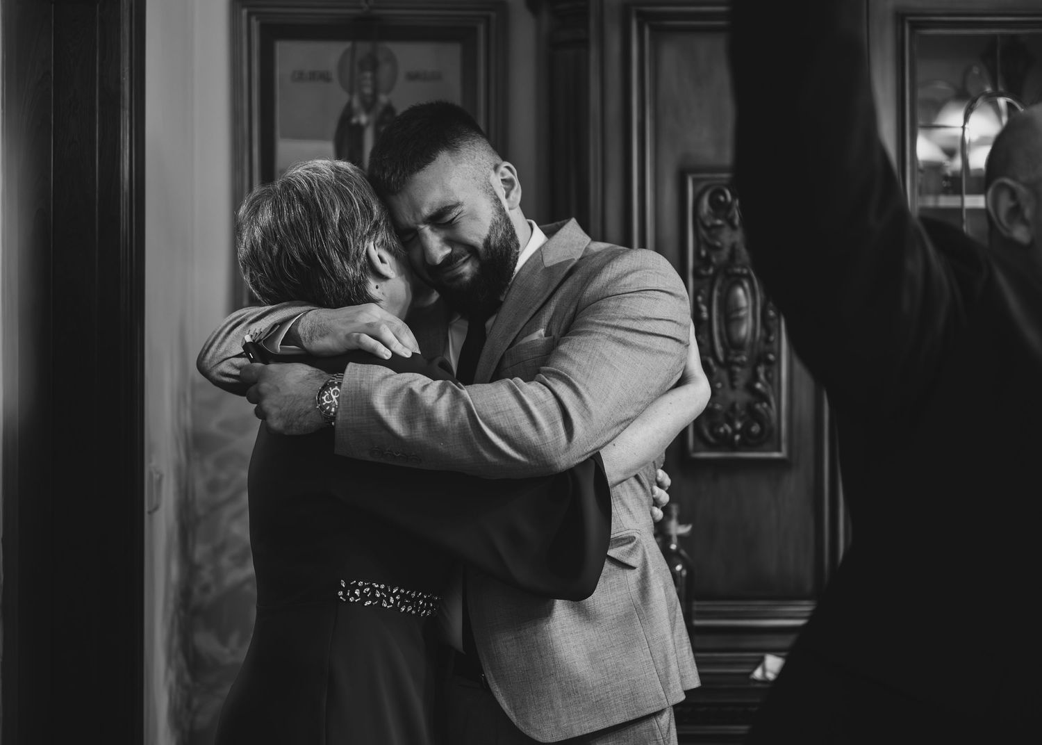 Two men sharing a heartfelt hug indoors in an emotional black and white wedding moment.