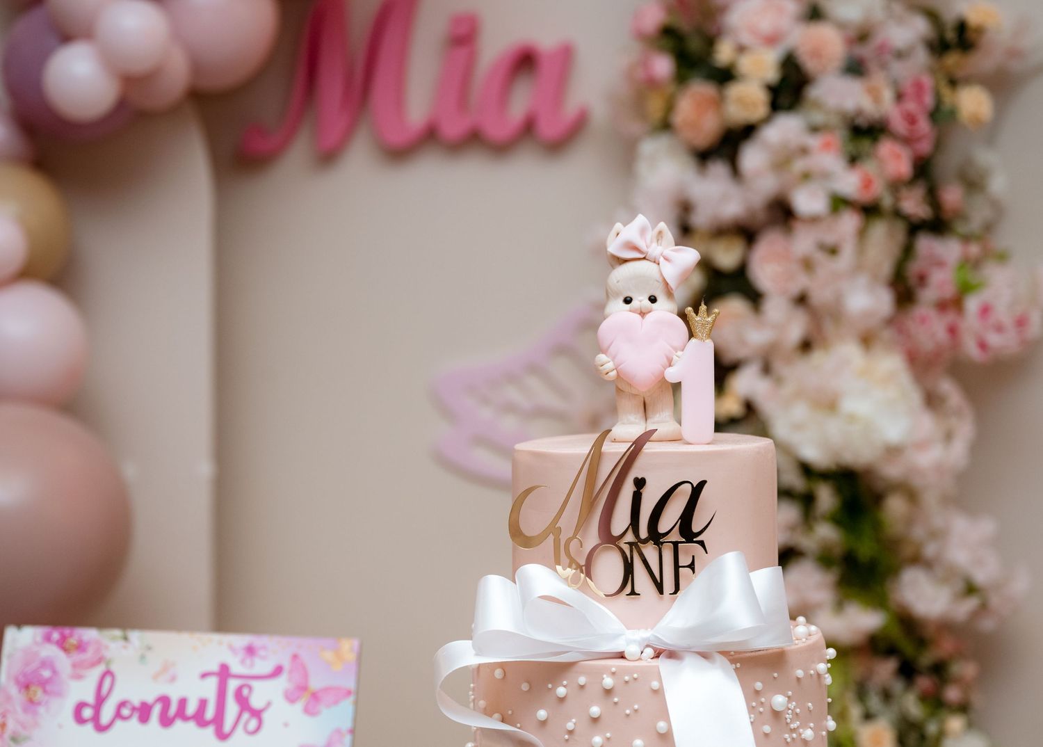 Pink first birthday cake topper with bunny holding heart for baby Mia's ONE celebration.