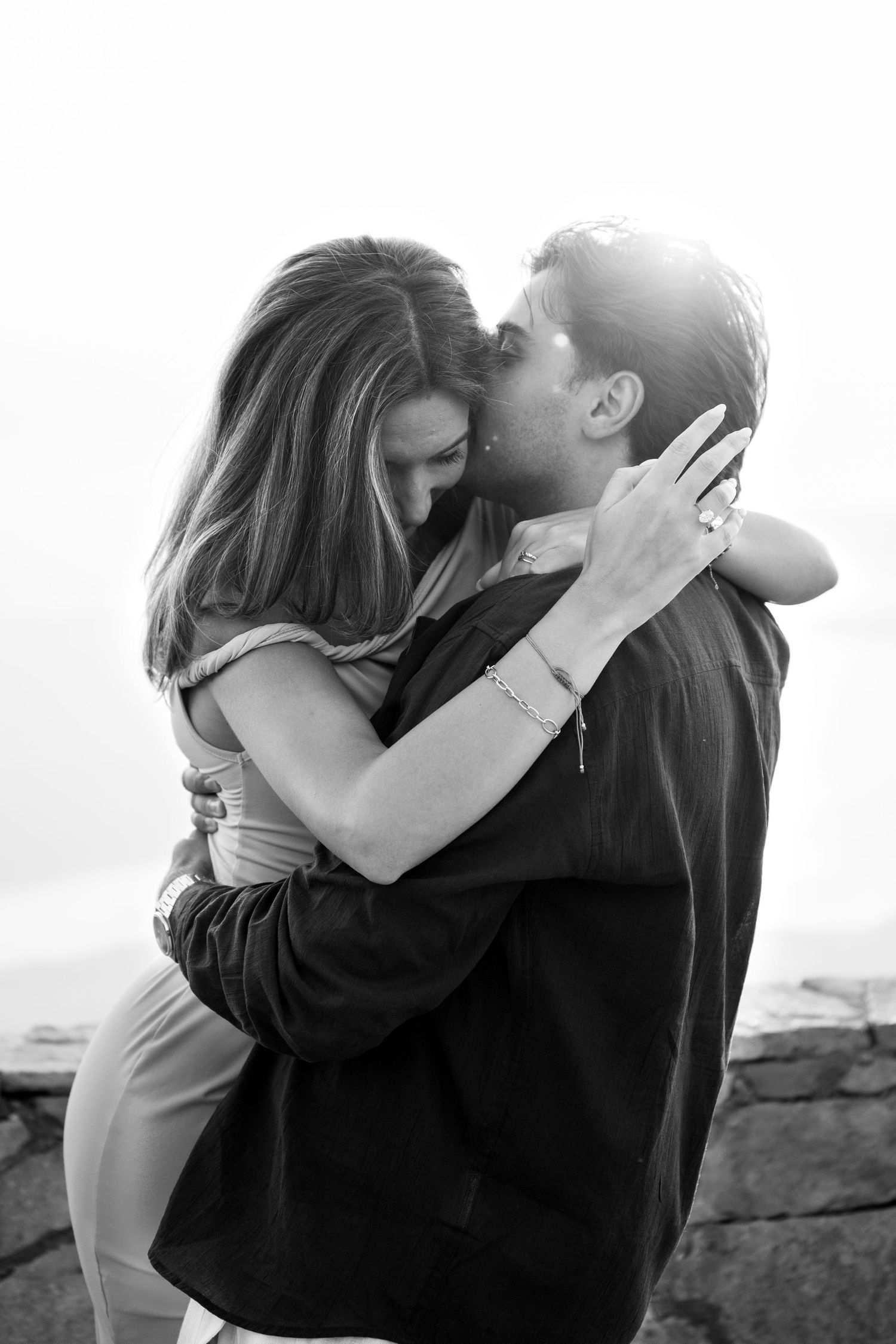 Black and white romantic photo of a couple sharing a tender embrace with backlit glow.
