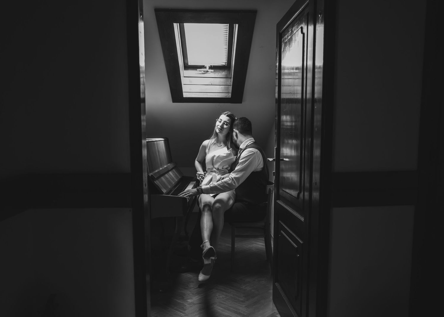 Black and white intimate photo of bride and groom sharing a tender moment by a piano.