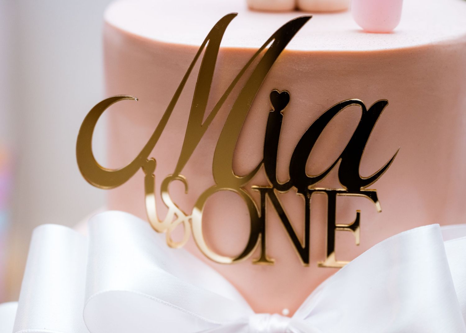 Gold acrylic Mia One cake topper on a pink first birthday celebration cake.